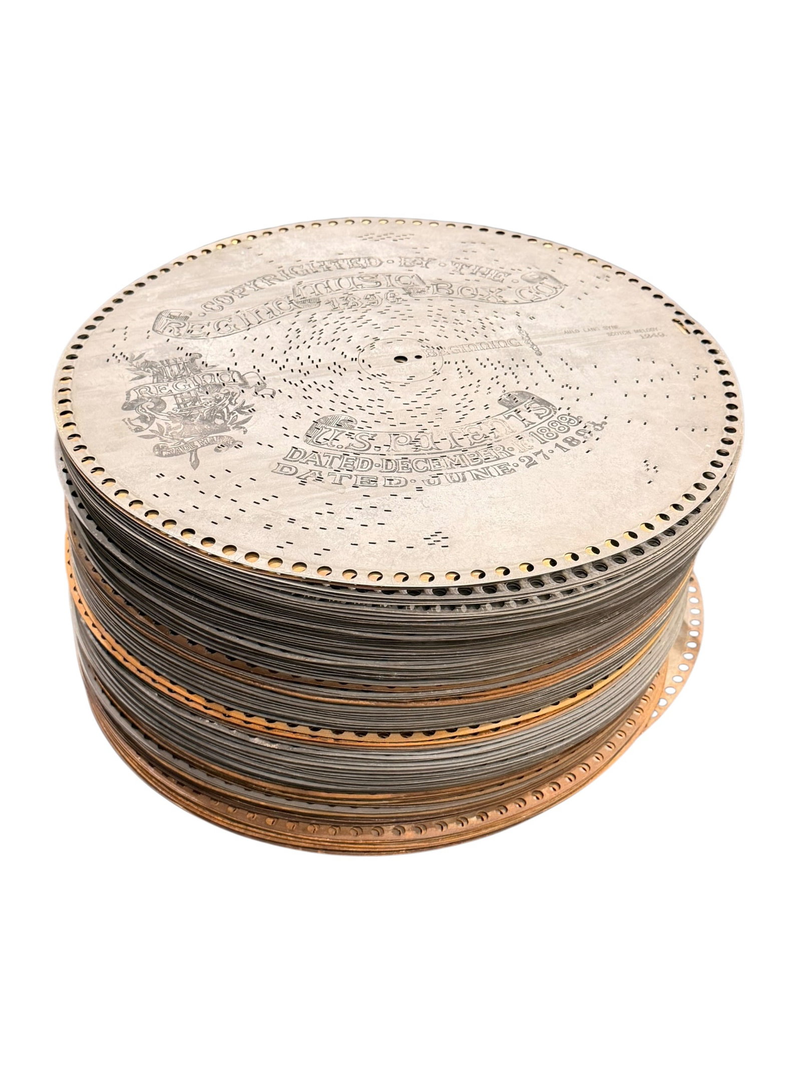 Lot of 100 Music Box Discs: The image shows a stack of vintage metal music box discs manufactured by the Regina Music Box Company, featuring visible patent dates from 1889 and 1893 stamped on the top disc surface. [1]Item Type: 