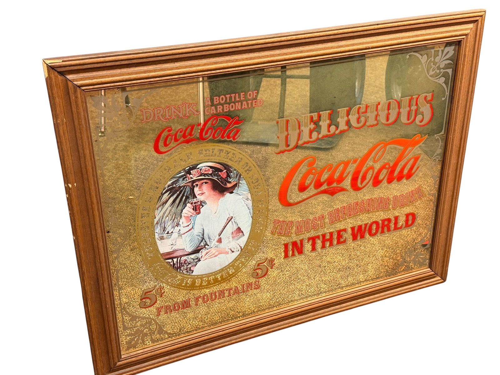 Coca Cola Advertising Mirror: This image appears to show a vintage wood-framed Coca-Cola advertising mirror featuring a turn-of-the-century lady graphic and "Delicious Coca-Cola in the World" text. [1, 2]Appears to be a retro