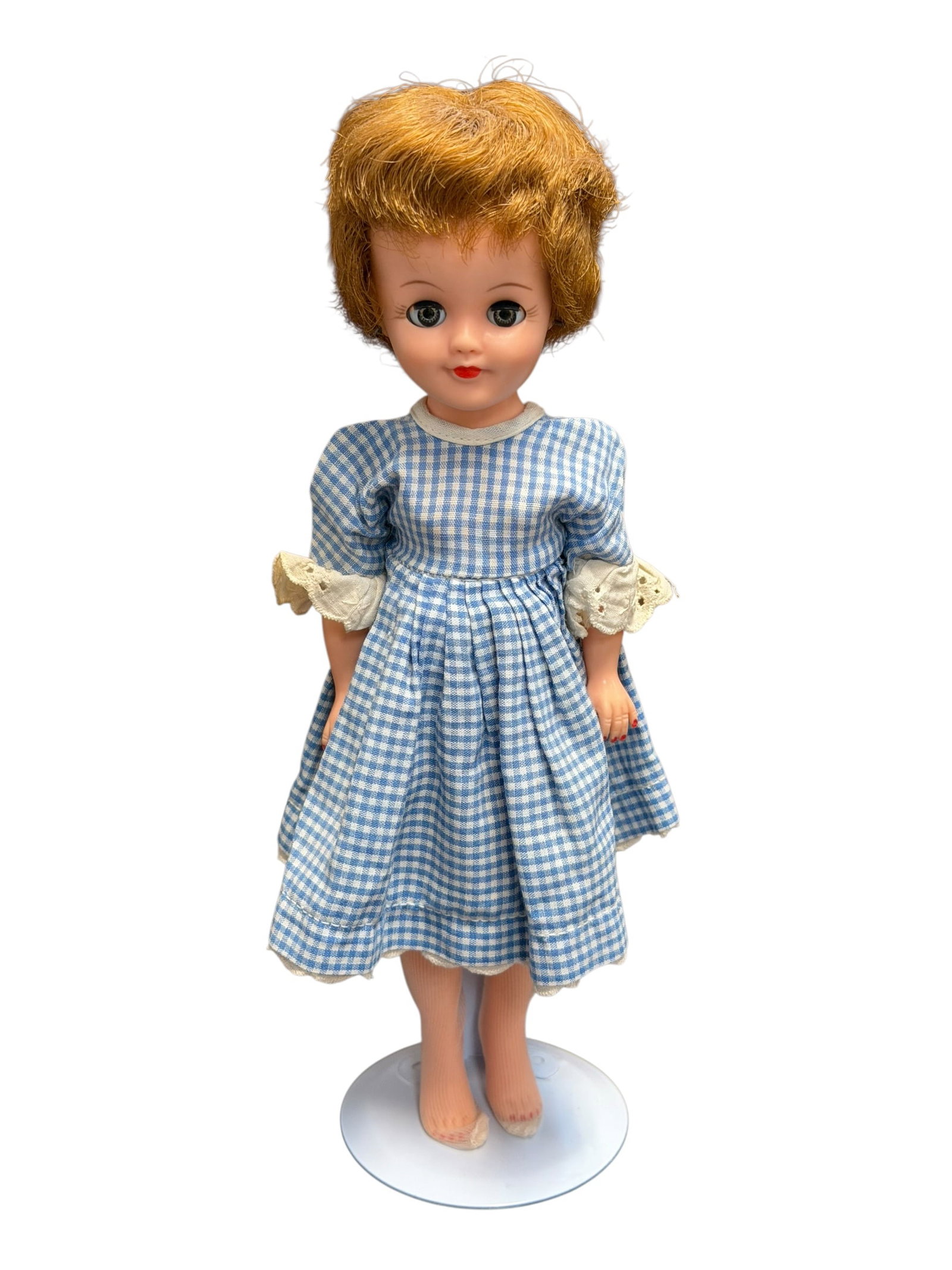 Vogue Vinyl Doll: vintage plastic fashion doll from the mid-20th century, resembling styles from makers like Madame Alexander or similar era companion dolls, wearing a blue and white gingham dress with lace-trimmed