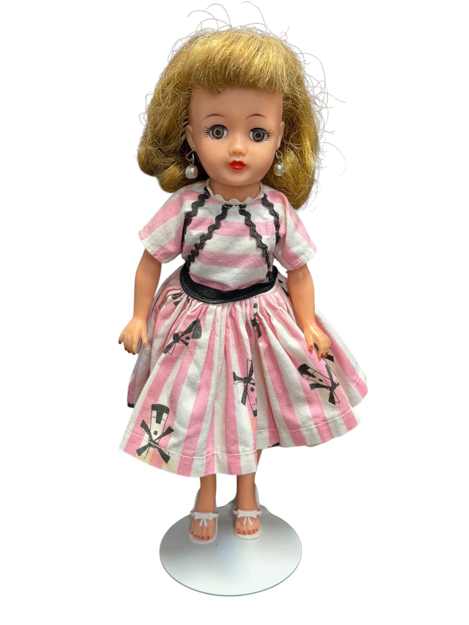 Ideal Vinyl Doll: This is a vintage 1958 Ideal Little Miss Revlon doll, standing on a display base. [1]She is wearing her highly sought-after, original #9056 Windmill Print Dress, which features iconic pink and white