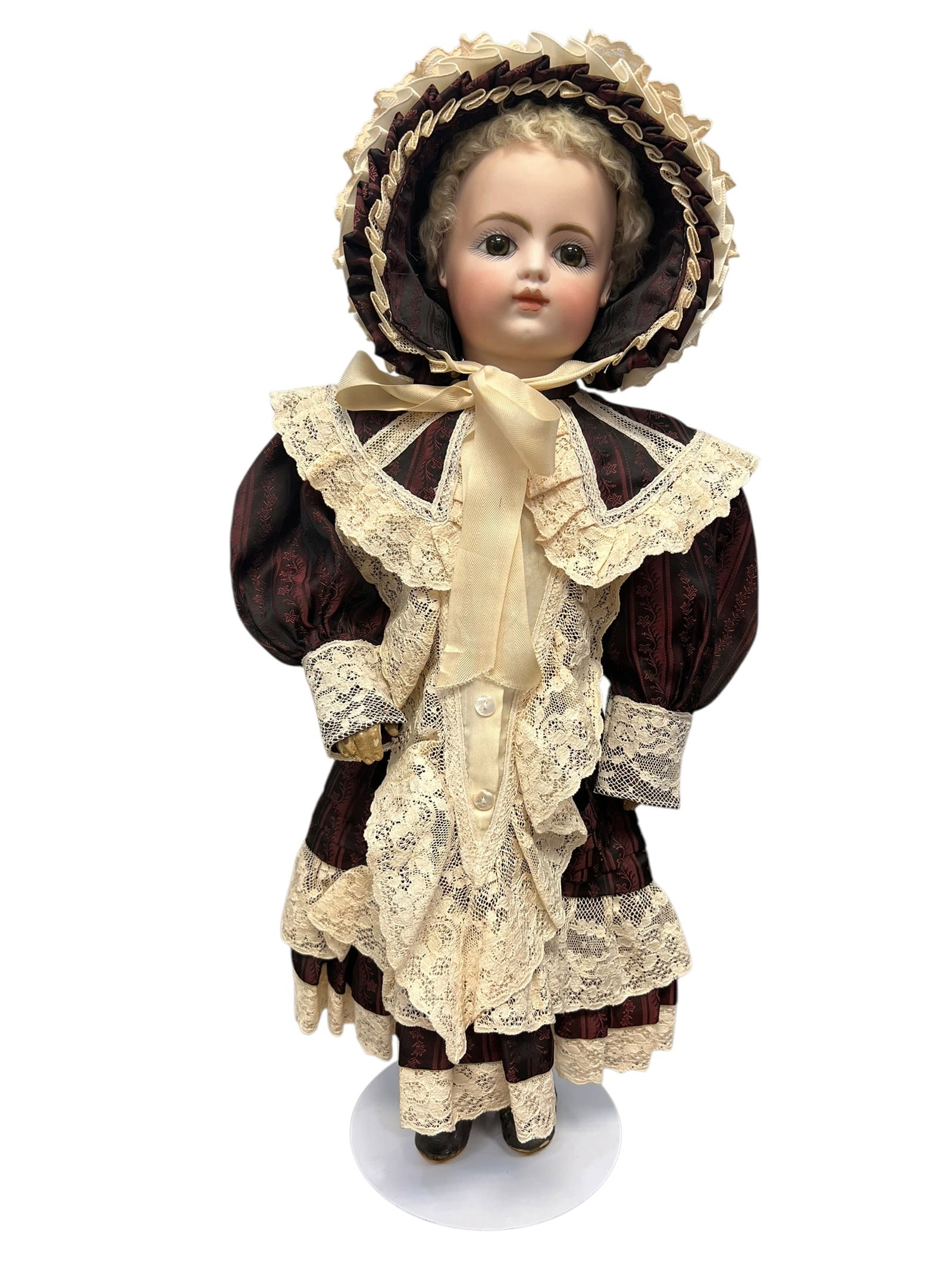 F. 7. G. Bisque Head Doll: antique bisque-head doll, likely of German or French manufacture from the late 19th or early 20th century, dressed in a burgundy and lace outfit with a matching bonnet.It features a pale bisque