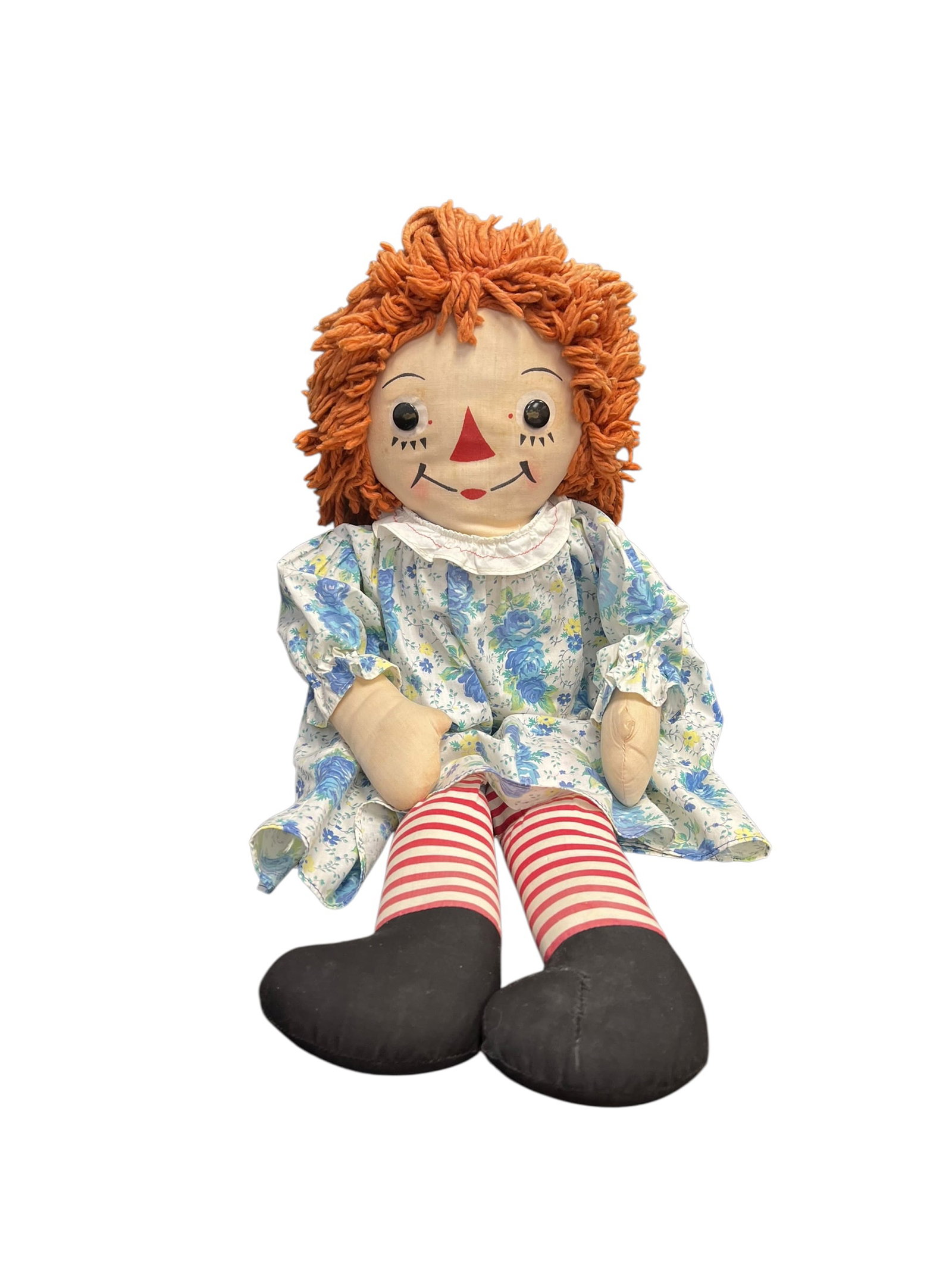 Raggedy Anne Doll: This image shows a vintage Raggedy Ann cloth doll with characteristic red yarn hair, a printed face featuring black button-like eyes and a triangular nose, a blue floral dress with a ruffled collar,