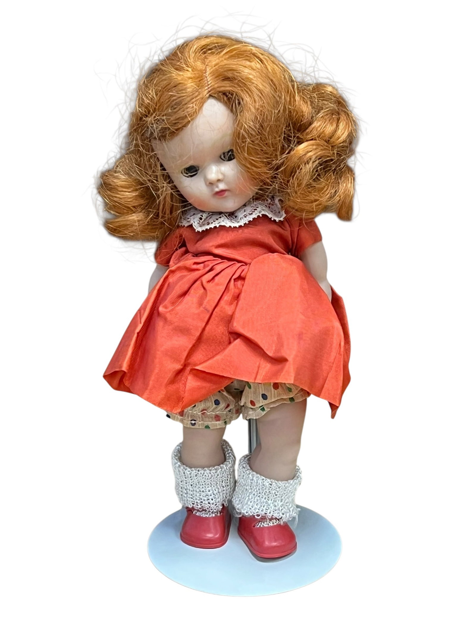 Vogue Plastic Doll: vintage 8-inch hard plastic Vogue Ginny doll from the 1950s, featuring red side-curled hair, a bright orange-red dress with white lace trim, patterned polka-dot bloomers, textured white socks, and red