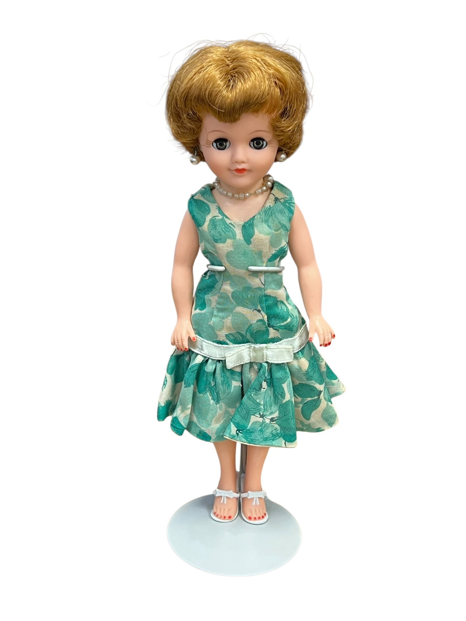 Vogue Vinyl Doll: vintage mid-century fashion doll, closely resembling a 1950s Ideal "Miss Revlon" or similar ball-jointed/poseable doll wearing a teal floral-pattern sleeveless dress, pearl necklace, and white sandals
