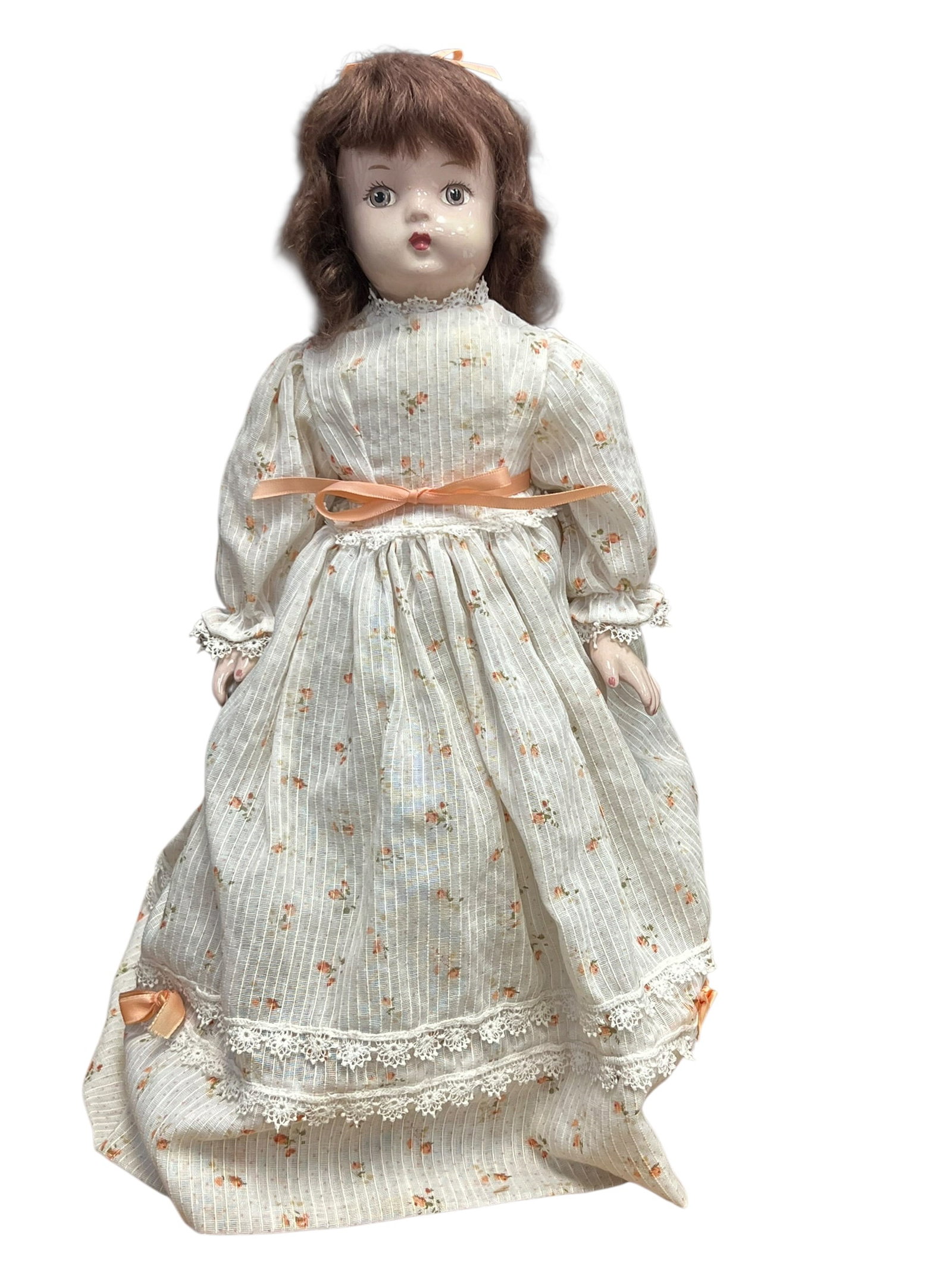 Porcelain Head Doll: vintage decorative porcelain collector doll wearing a cream-colored floral dress with lace trim and an orange ribbon.Doll FeaturesFace and Head: Crafted from painted porcelain with molded facial featu