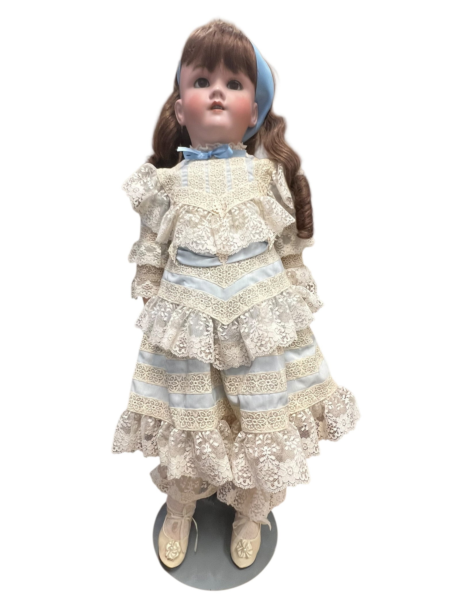 Handwerck Germany Bisque Head Doll: antique or vintage bisque porcelain doll styled with brown wavy hair, a blue headband, and a multi-tiered cream lace dress accented with light blue ribbons