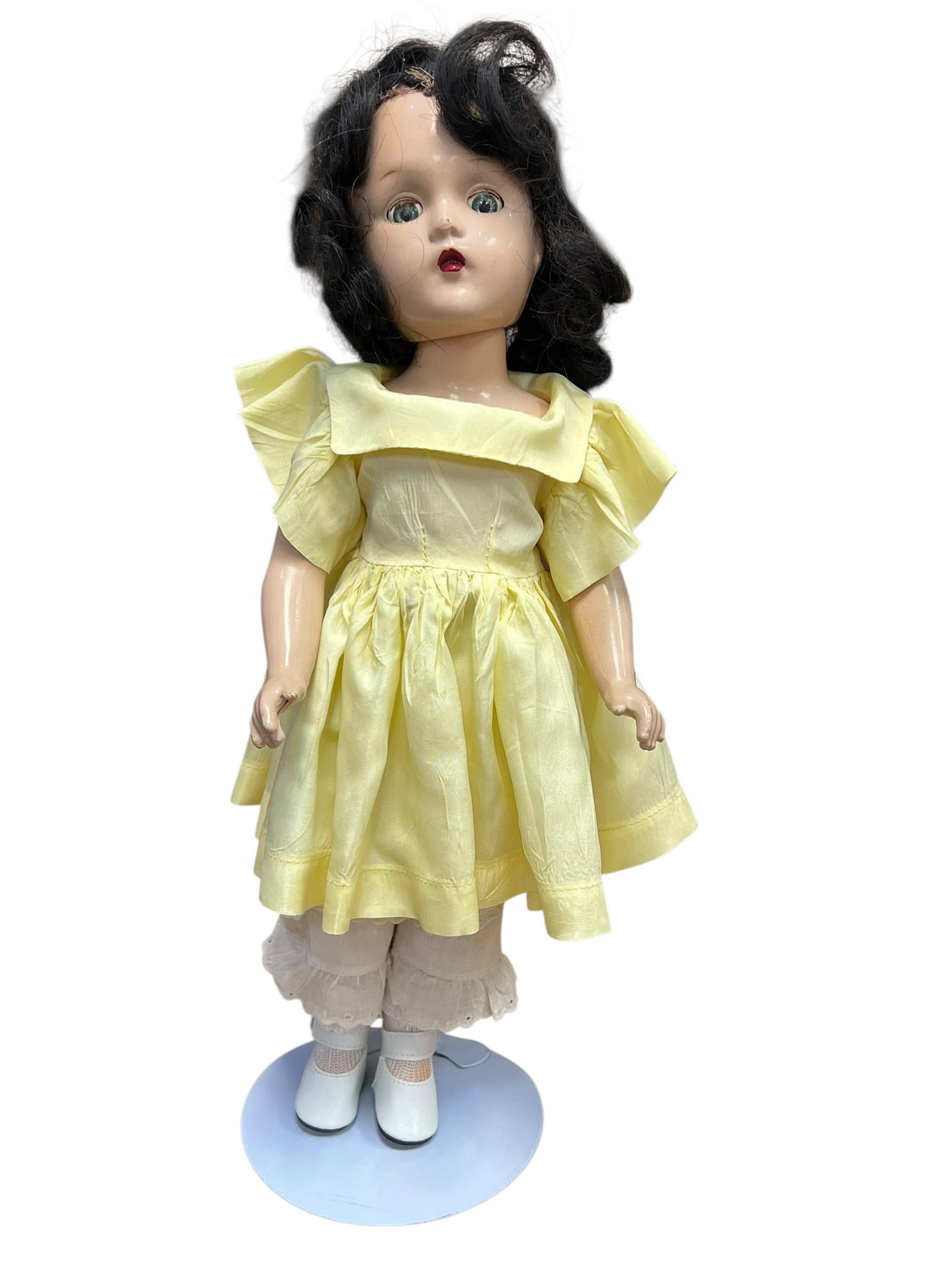 Madame Alexander Doll: vintage composition or hard plastic doll, possibly from the mid-20th century, wearing a yellow dress and white shoes. [1, 2]Style: Features dark wavy hair, painted facial features with red lips, and