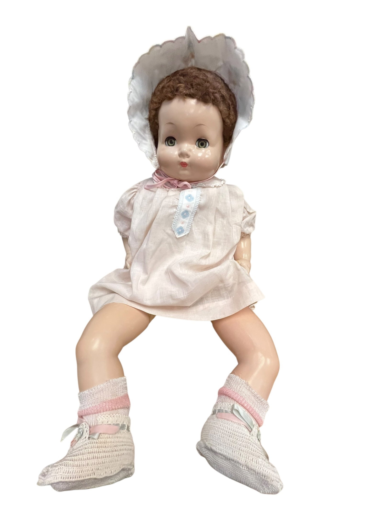 Effanbee Composition Doll: vintage baby doll with brown hair, blue sleep eyes, wearing a white bonnet, light pink dress, and knit booties, resembling a mid-20th-century composition or hard plastic doll like an Effanbee or simil