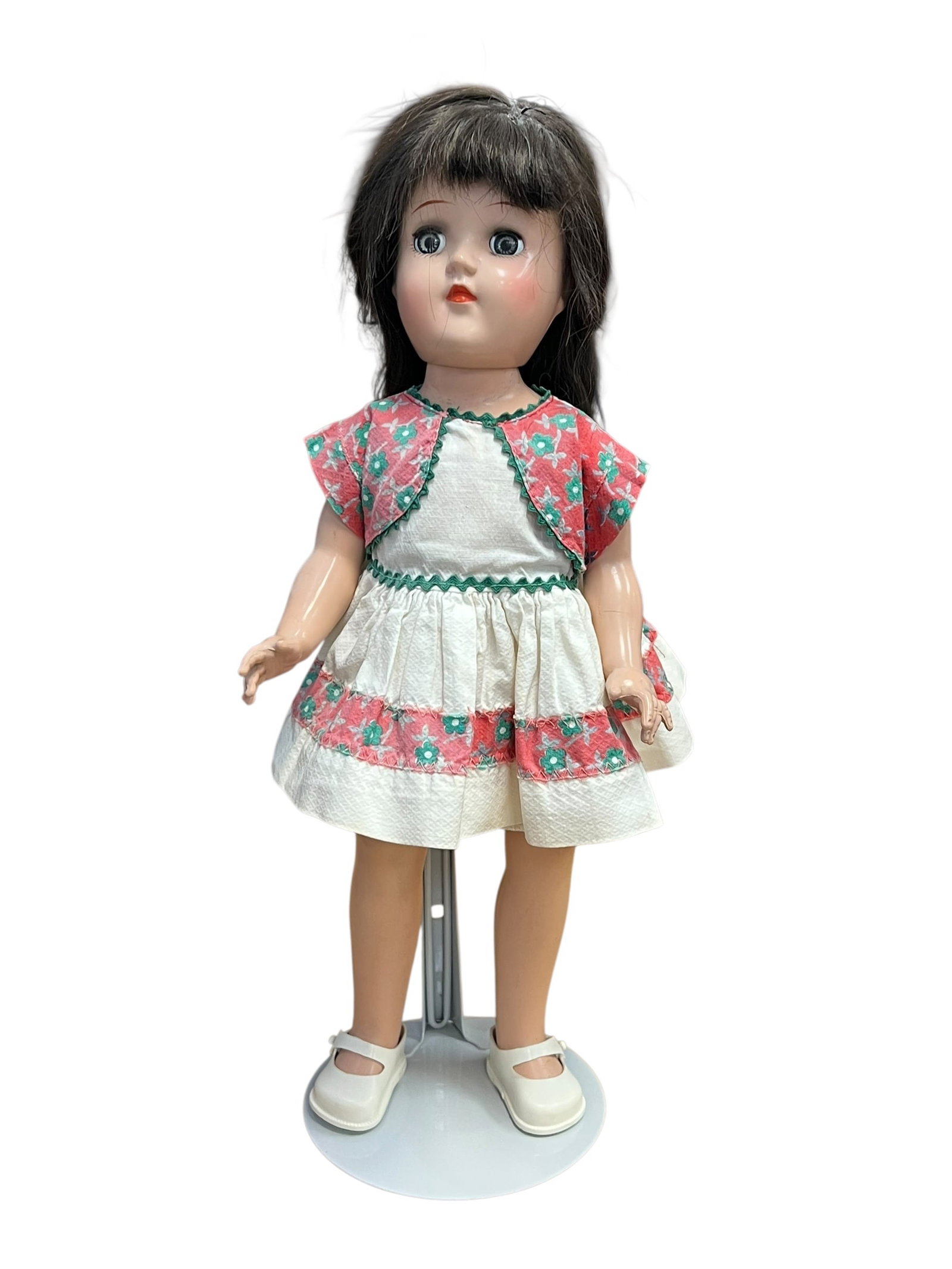 Ideal P-90 Doll: vintage Ideal P-90 Toni hard plastic doll from the 1950s, wearing a floral-trimmed dress and matching vest. [1, 2]Era: Manufactured during the 1950s by the Ideal Toy Corporation.Material: Crafted from