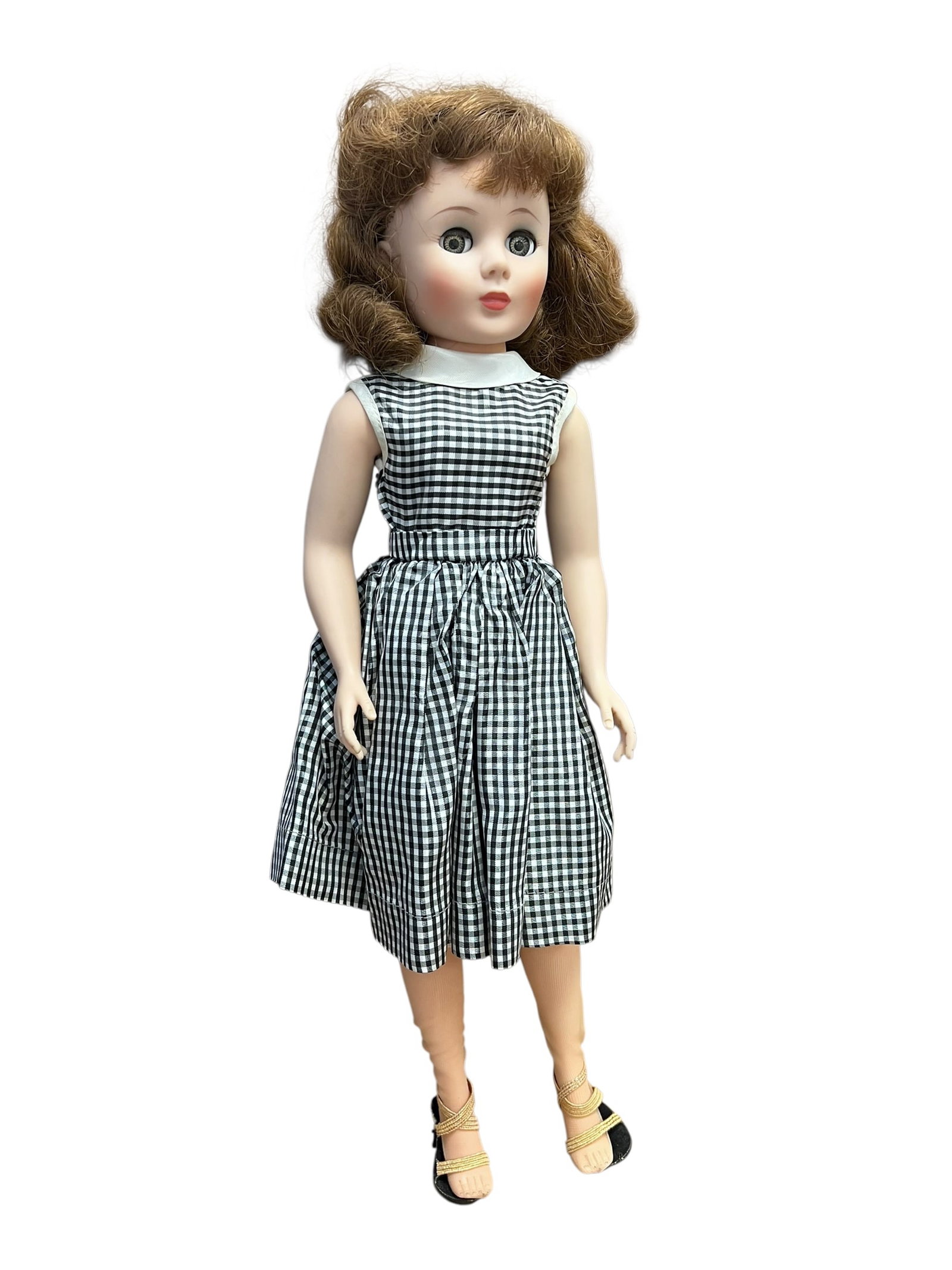 Bisque Head Doll: This appears to be a vintage 1950s hard-plastic fashion or walker doll wearing a classic black-and-white gingham dress. [1, 2]Doll FeaturesHair: Styled brown bob with soft waves around the face.Body: