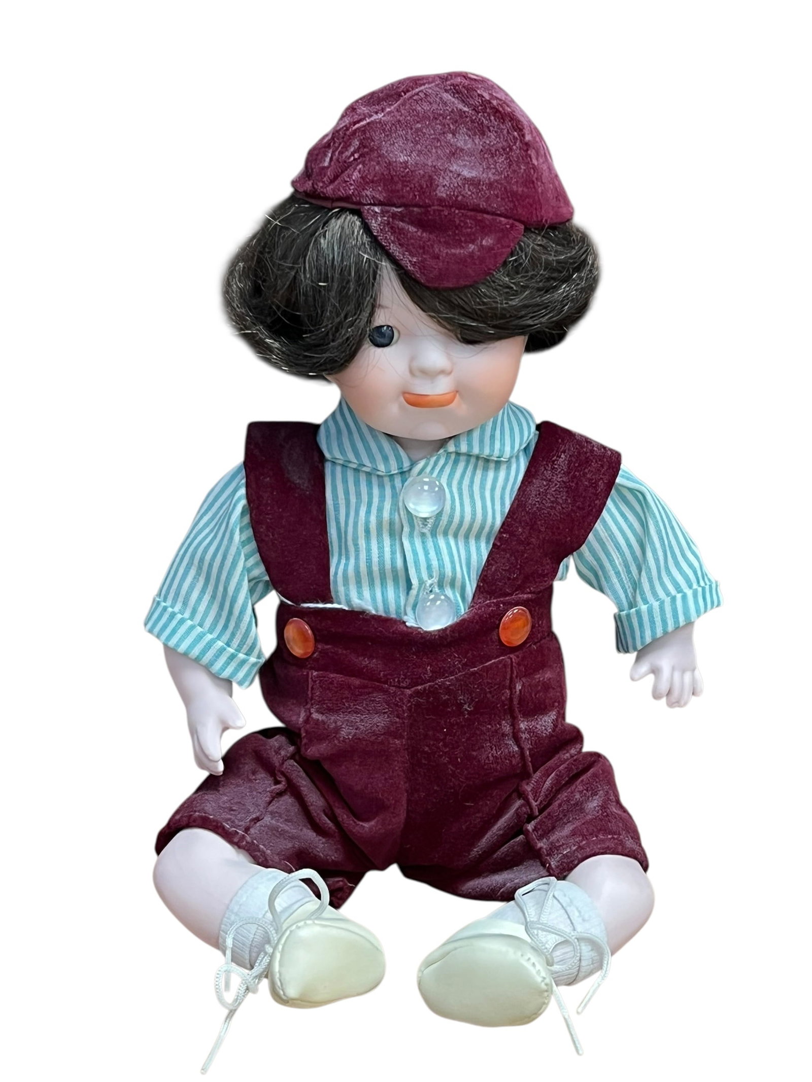 Bisque Head Doll: This appears to be a vintage collectible porcelain boy doll with dark hair, wearing a striped shirt, velvet-style burgundy overalls, matching cap, and white lace-up shoes.