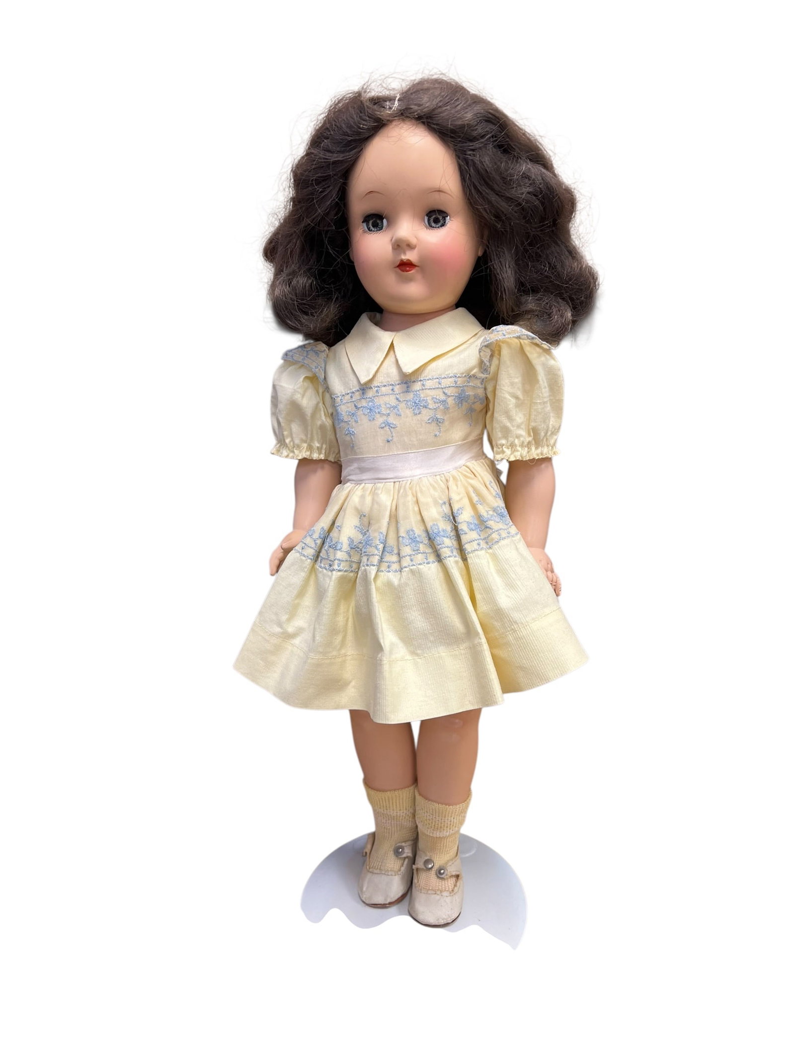Ideal Plastic Doll: vintage hard plastic doll, closely resembling a mid-century Ideal Toni or a similar fashion/character doll from the 1940s to 1950s, styled with dark wavy hair, sleep eyes, and a pale yellow smocked dr