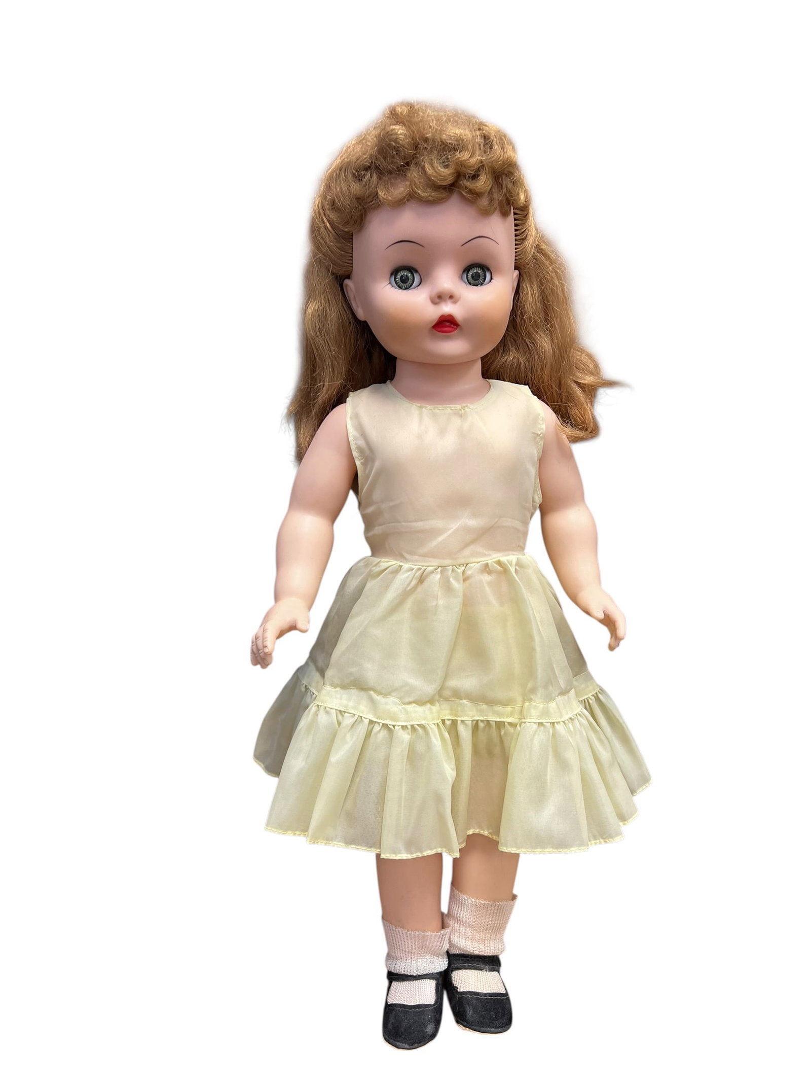 Vinyl Doll: This is a vintage hard plastic doll from the mid-20th century. It features auburn hair, sleep eyes, and a classic 1950s style. The doll is wearing a light yellow sleeveless nylon dress with a ruffled