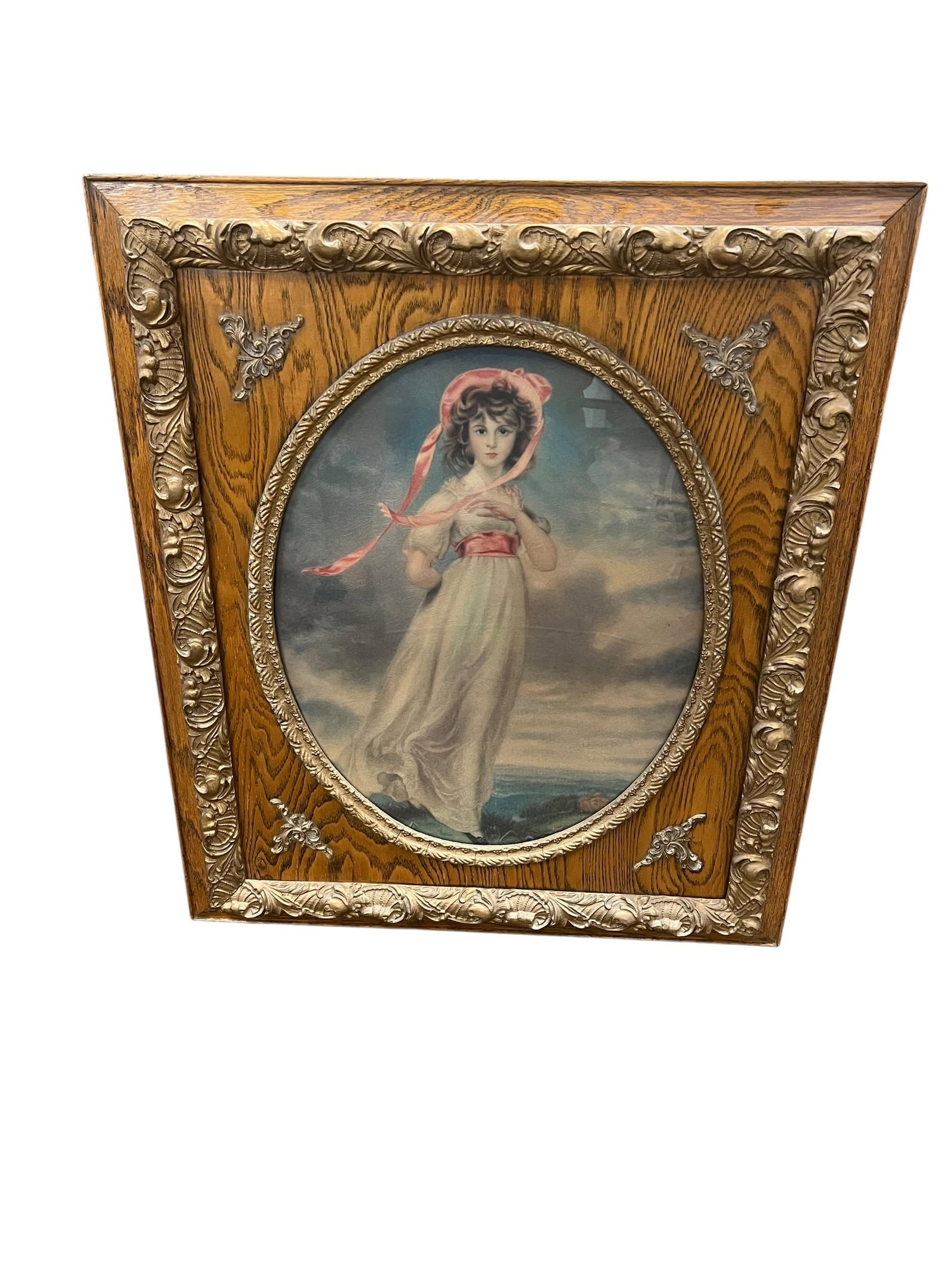 Antique Framed Portrait Print of Young Woman in Bonnet – Ornate Oak & Gilt Frame: Antique decorative portrait depicting a young woman in a flowing white Empire-style dress with a pink sash and bonnet, posed against a dramatic landscape and cloudy sky. The oval portrait is housed be