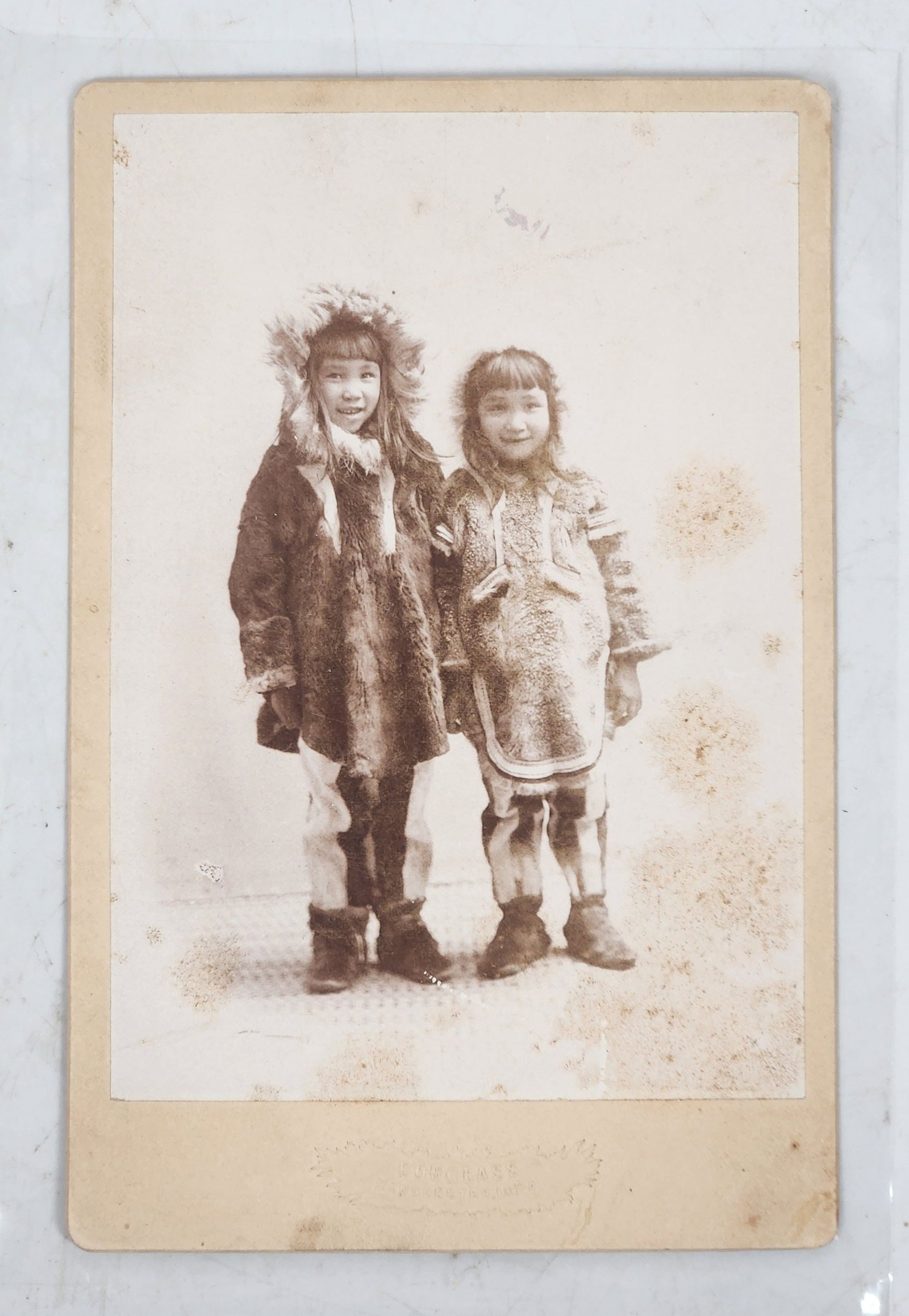 Vintage Inuit Children Cabinet Photograph - Arctic Culture: This is a vintage photograph of two children in traditional clothing. Based on the style of dress and the fur-lined hoods, they may be Inuit or from another Arctic culture. The photo is mounted on car