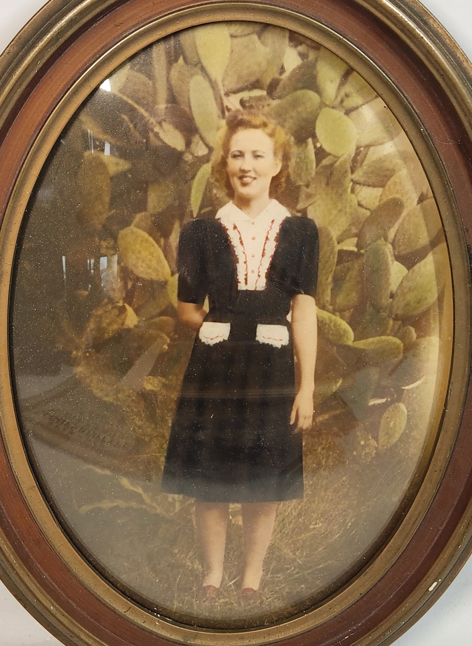 Oval Framed Photo - Woman in Dark Dress, 13.5" Tall: This is an oval framed picture of a woman. The frame is brown, 13.5" tall, 11" wide, and 1" thick. The picture is of a woman in a dark dress with white accents, in front of what looks like a cactus. T