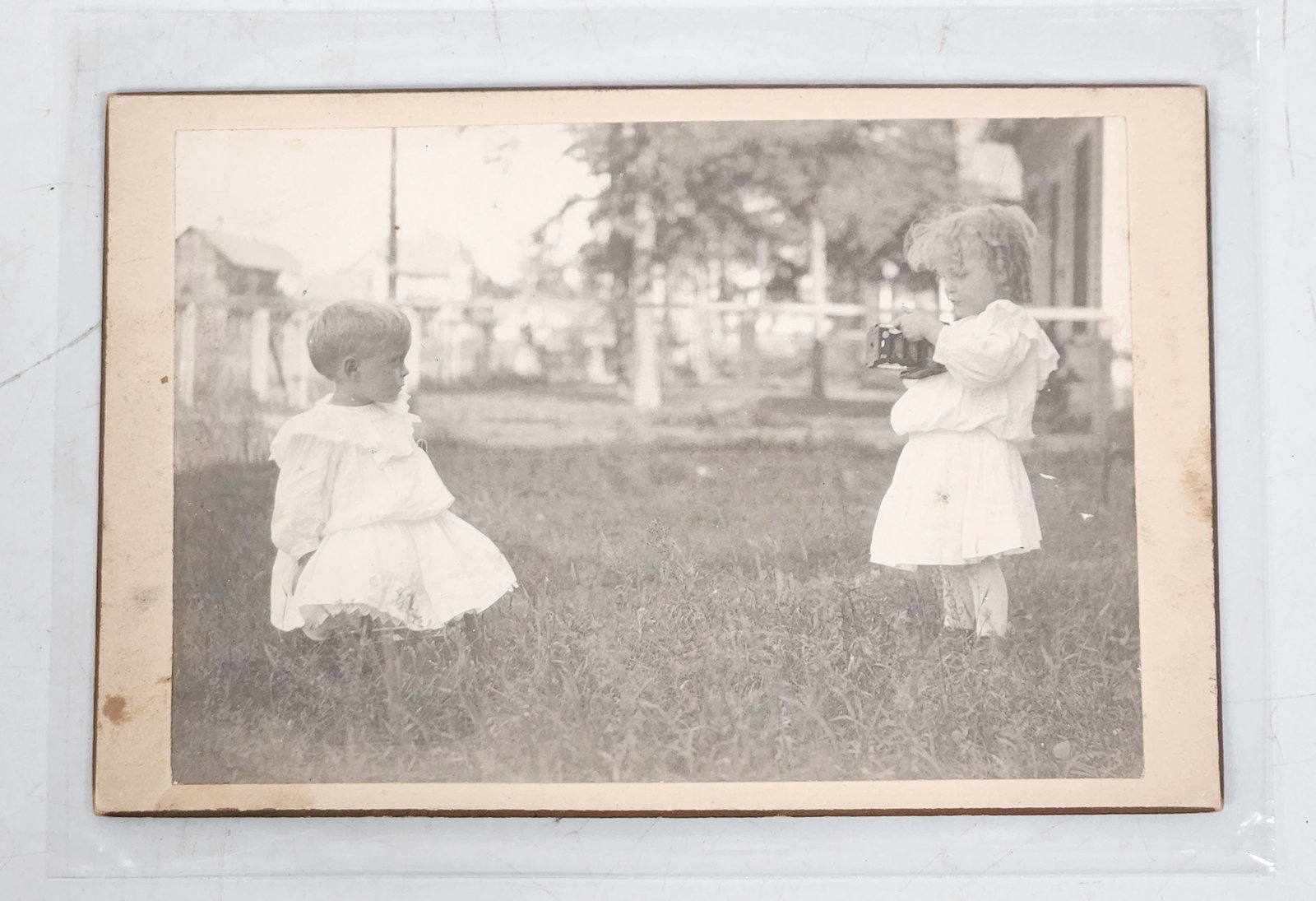 Antique Photograph - Children with Camera - 6" x 4": Antique photograph of two children in white dresses. One of the children is holding a camera. The photograph has a cardboard backing. Dimensions are approximately 6" x 4".height: 6 inches (Photograph)