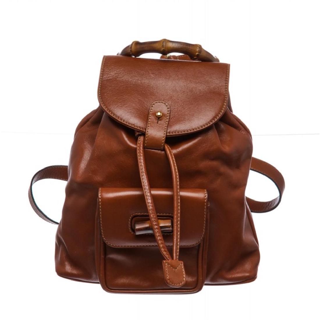 Gucci Brown Leather Drawstring Bamboo Mini Backpack: Overall flap push tab and drawstring closure. Interior contains fabric lining with one zipper pocket. Exterior contains adjustable straps, leather pocket with bamboo twist lock and handle. Item is Pre