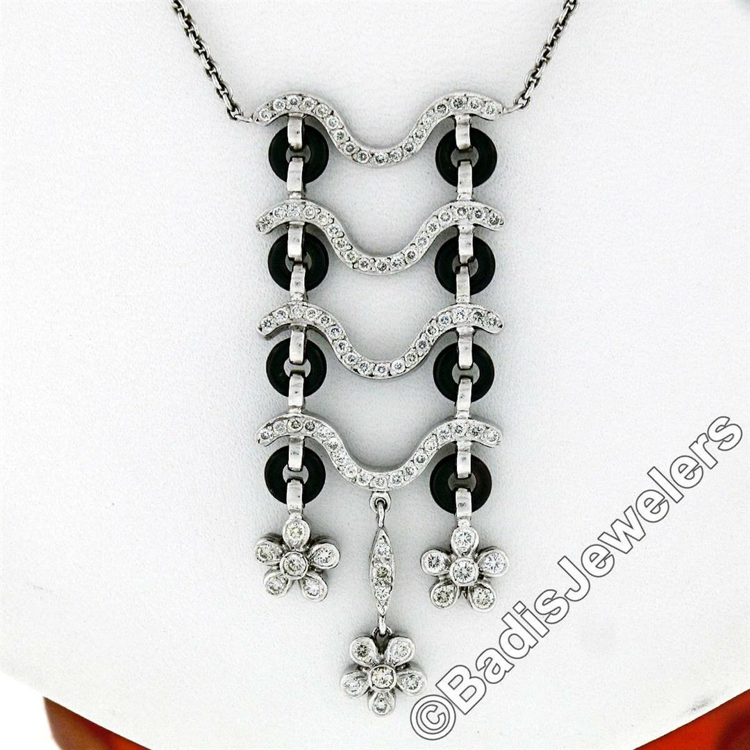 18kt White Gold 1.15 ctw Black Onyx and Diamond Flower: An 18kt white gold floral motif tassel pendant necklace with 8 custom round cut 5.0mm black onyx stones and 1.15ctw of round brilliant cut diamonds (F/G - VS1/VS2). 16 inch cable link chain, 10.87 gra