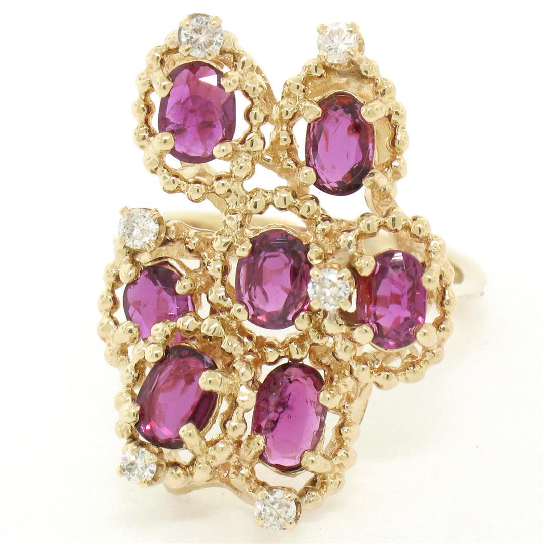 14kt Yellow Gold 2.14 ctw Ruby and Diamond Cluster: A 14kt yellow gold cluster cocktail ring featuring 1.96ctw of oval cut rubies accented by 0.18ctw of round brilliant diamonds (F/G - SI1). The ring is size 7.0, weighs a total of 6.49 grams, and measu
