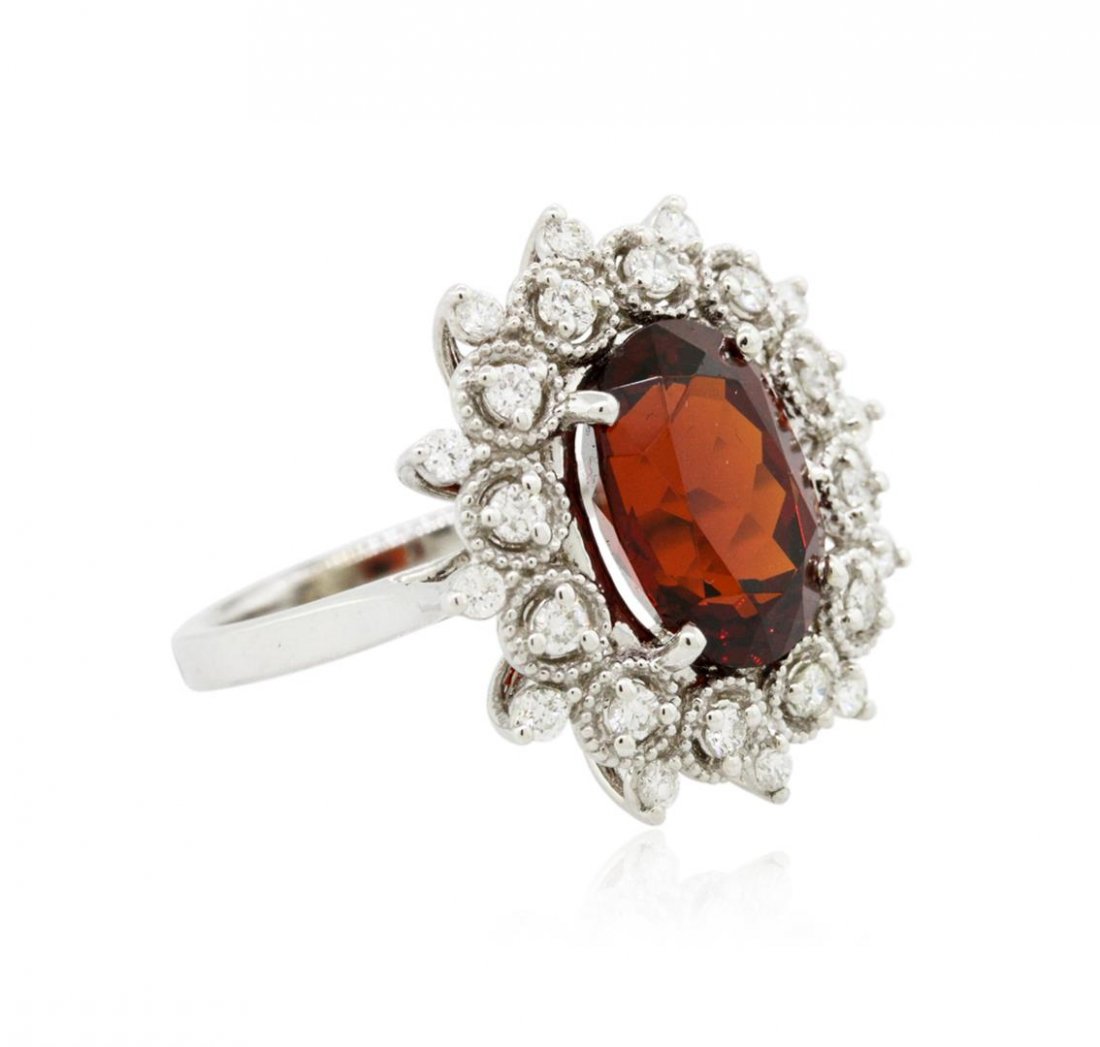 14KT White Gold 5.43ct Spessartite and Diamond Ring: One electronically tested 14KT white gold ladies cast spessartite garnet and diamond ring. The featured spessartite garnet is set within a stylized diamond floret bezel, completed by a two millimeter 