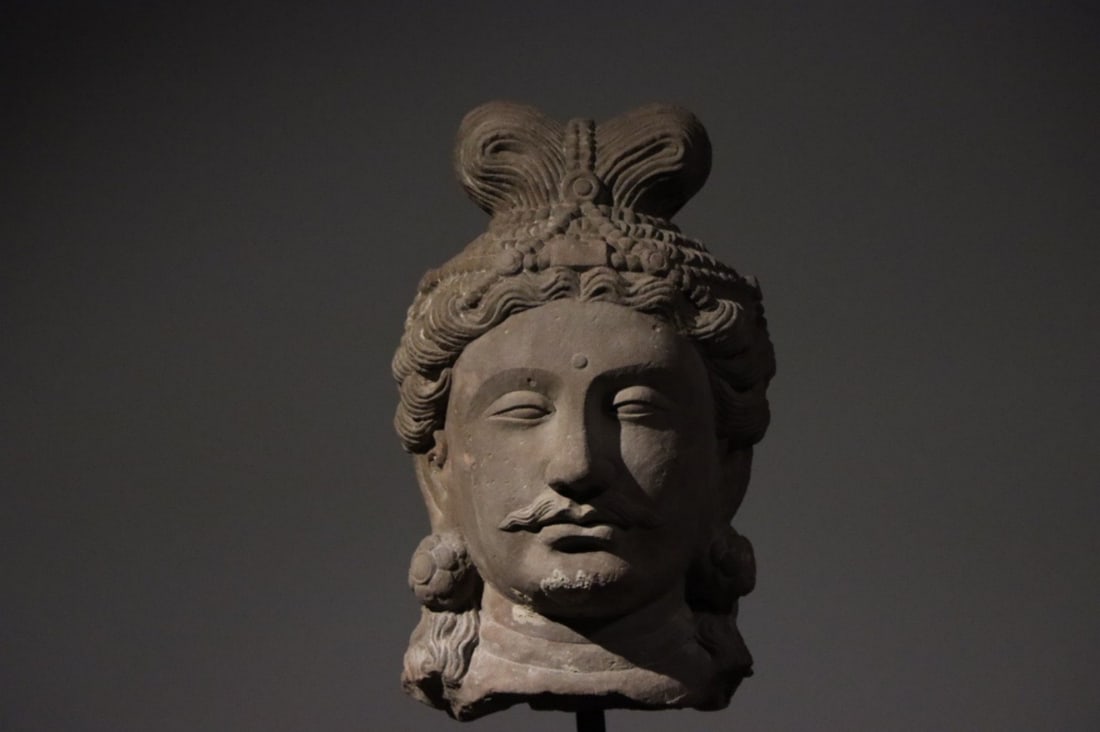 2nd-3rd Century: Gandhara Art Sculpture: Material: Red Sandstone; Height: 40cm (Height: 15.75")This Gandhara (2nd–3rd CE) red sandstone god head (peak Gandhara art): jewel crown, calm face, beard, floral earrings, Greek-style curly hair—