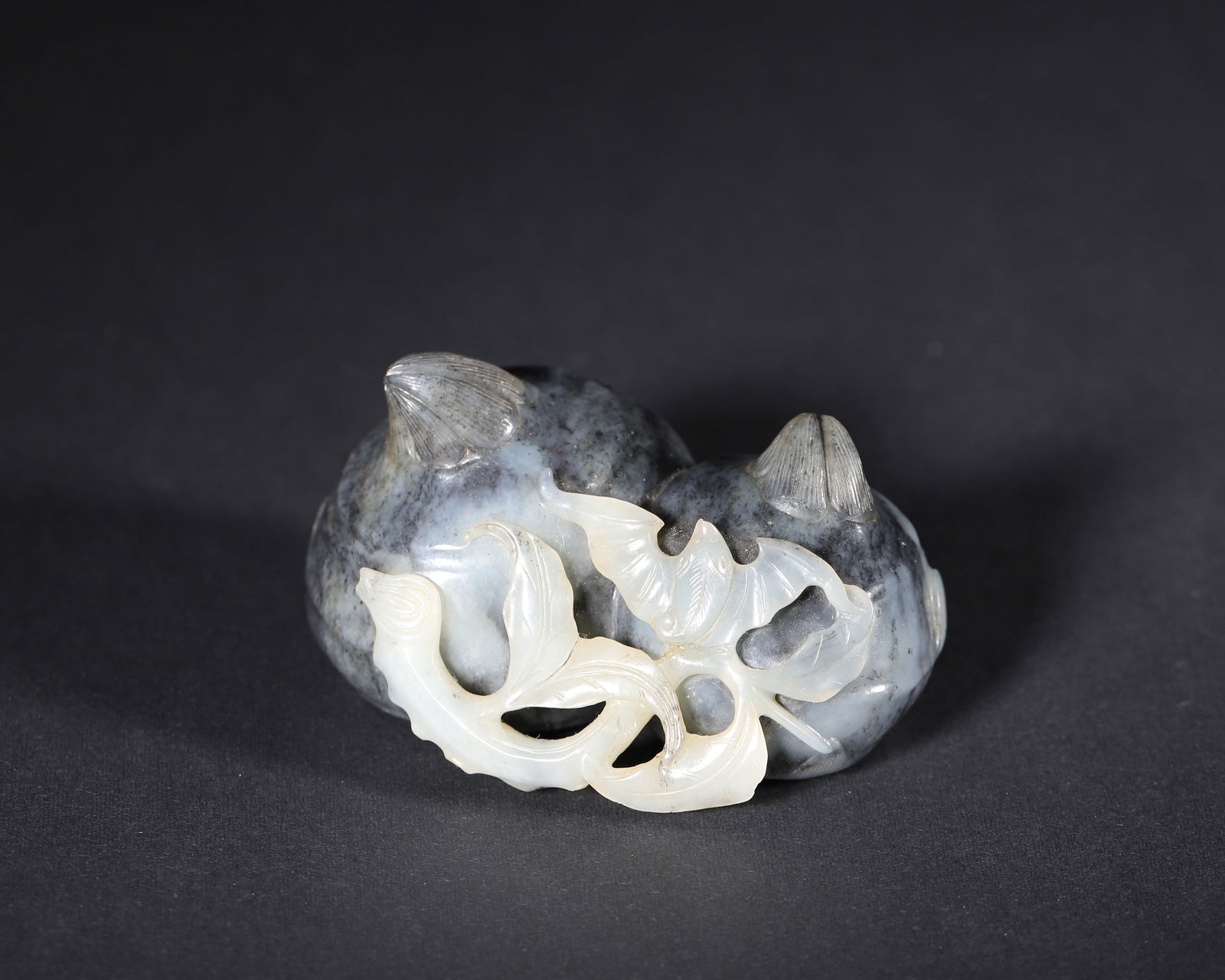 A Blue and White Hetian Jade Carving "Pomegranates and Bat" Ornament, Qianlong Period, Qing Dynasty: Length (L): 7.0cm (2.76in); Width (W): 5.0cm (1.97in); Height (H): 4.0cm (1.57in); Weight (Wt): 167.0g (0.37lb)This imperial ornament, made during the Qianlong period, is carved from blue and white