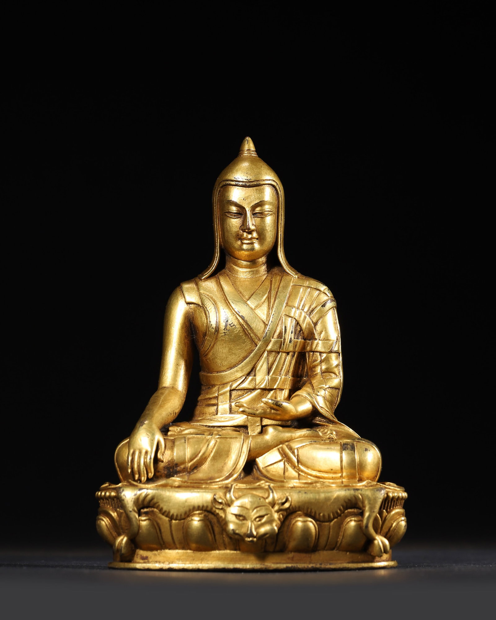 AN GILT-BRONZE FIGURE OF A LAMA, YONGLE PERIOD, MING DYNASTY: 3.94" x 3.15" x 5.91" inches (10.0 cm x 8.0 cm x 15.0 cm) | Weight: 1.36 lbs (619.0 g)A magnificent masterpiece from the Yongle court. Seated in bhumisparsha mudra, with a beast mask on the lotus base