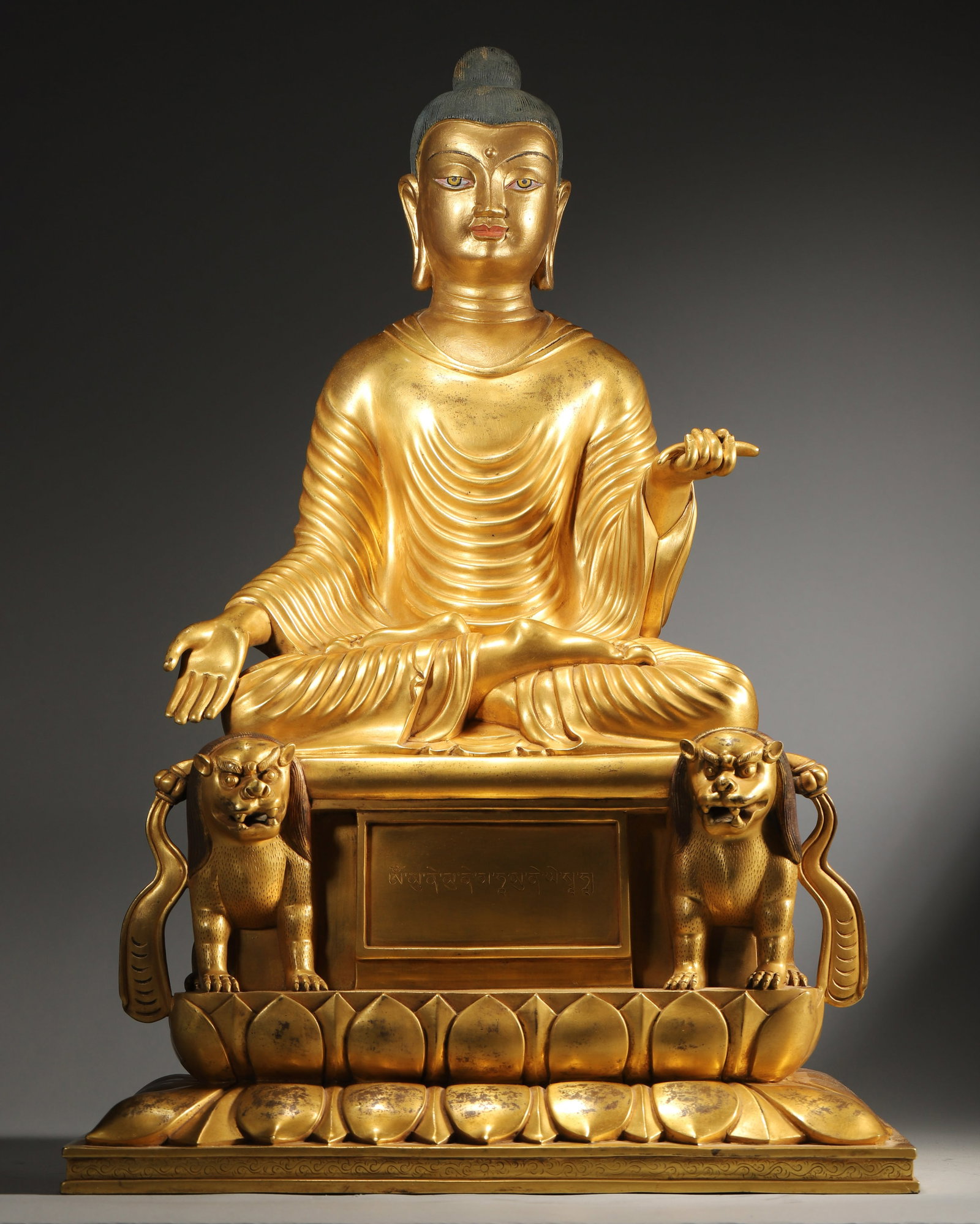 QING Dynasty GILT-BRONZE SAKYAMUNI Buddha Figure, 15th Century: 13.0" x 9.25" x 19.29" (33cm x 23.5cm x 49cm); 32.85 lbs (14900g). A fine gilt-bronze figure of Shakyamuni Buddha, seated in half-lotus posture on a double-lion lotus base, with Tibetan inscriptions a