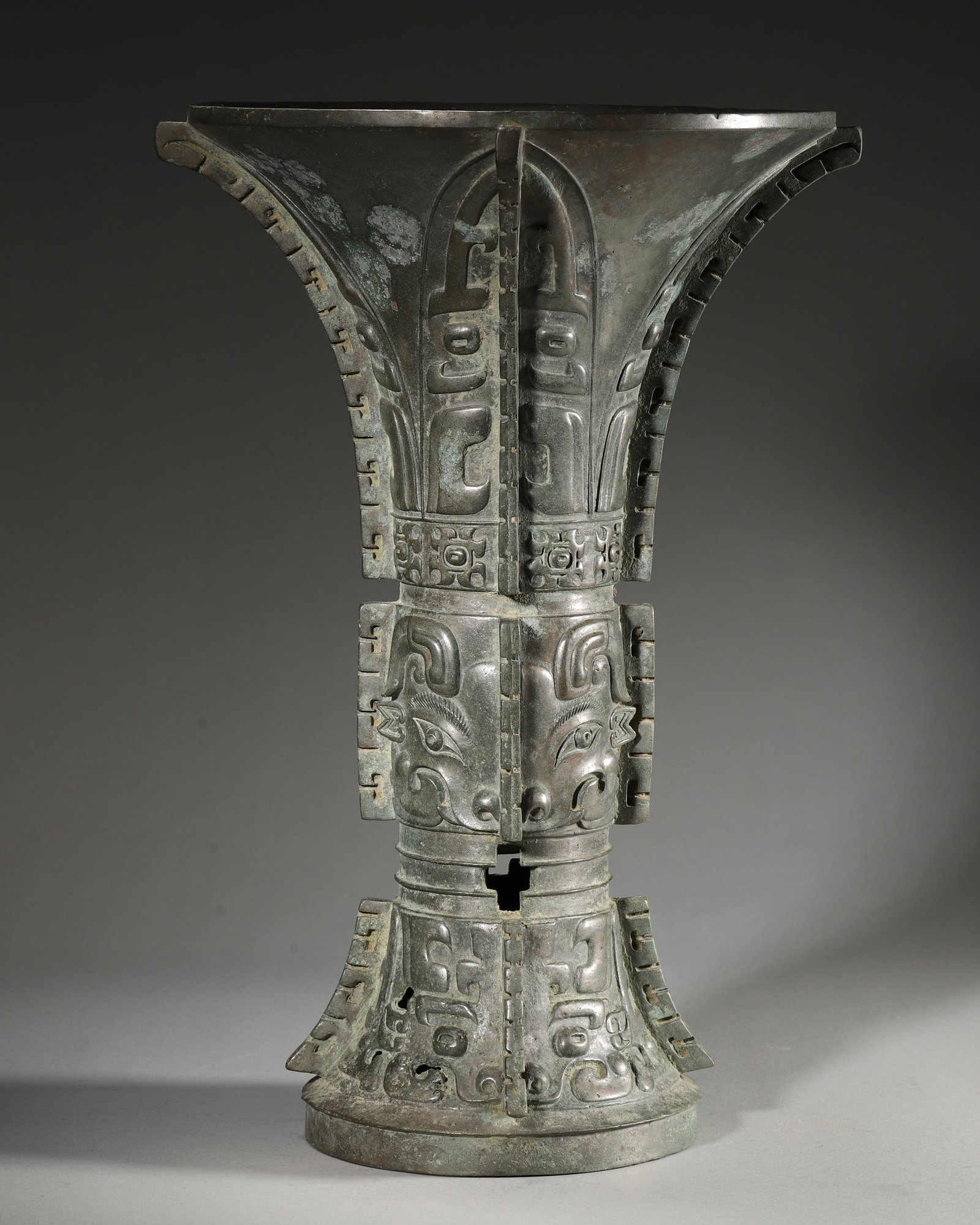 AN IMPORTANT ARCHAIC BRONZE RITUAL WINE VESSEL (GU), EARLY WESTERN ZHOU DYNASTY: D:24cm (9.45inches) H:35cm WT:4731g (10.43pounds)A fine archaic bronze ritual wine vessel (gu), Early Western Zhou dynasty, with prominent taotie masks, flanges, and an interior inscription, of excell