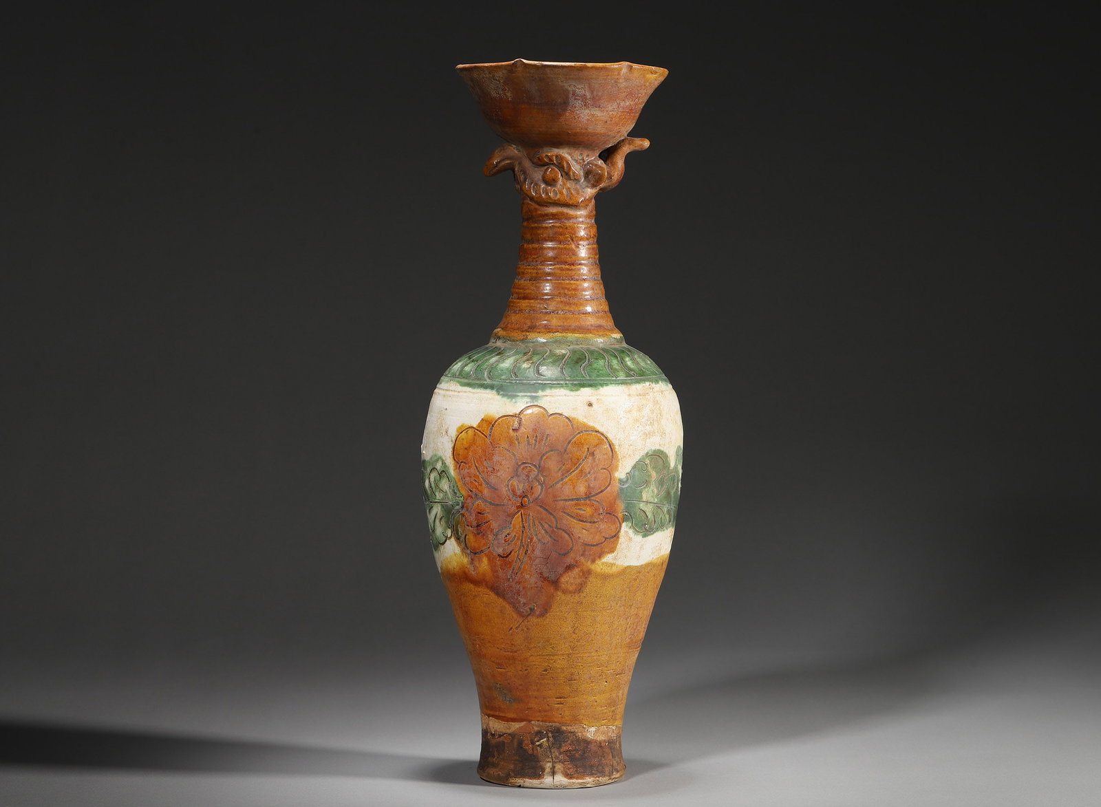SONG-JIN PERIOD, CIZHOU KILN SANCAI GLAZED VASE WITH MAKARA AND PHOENIX HEAD DESIGN: 4.72" x 12.99" inches (12.0 cm x 33.0 cm)This distinctive vase features a phoenix-head mouth, bamboo-joint neck, and incised peony motifs in vivid sancai glazes. The rare Makara decoration reflects th