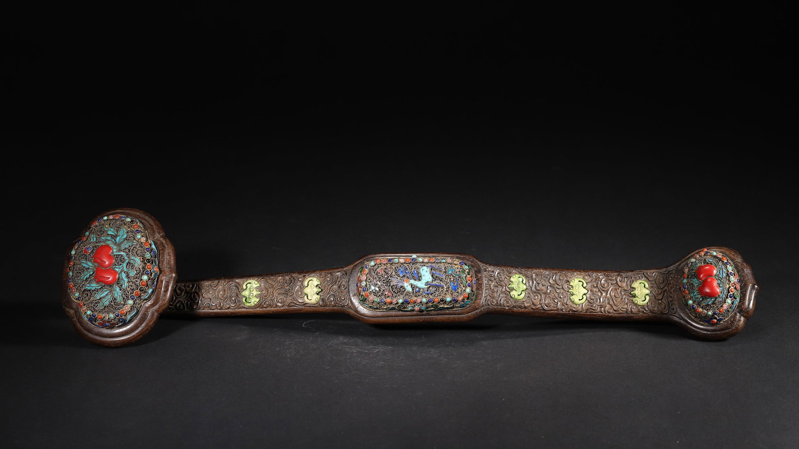 A ZITAN WOOD RUYI INLAID WITH GEMSTONES AND FILIGREE, QIANLONG PERIOD, QING DYNASTY: 18.12" x 3.88" (46.0cm x 1.0cm) | 0.90lbThis ruyi is carved from zitan wood, inlaid with turquoise and other gemstones, featuring exquisite filigree work and magnificent patterns. As an imperial ritua