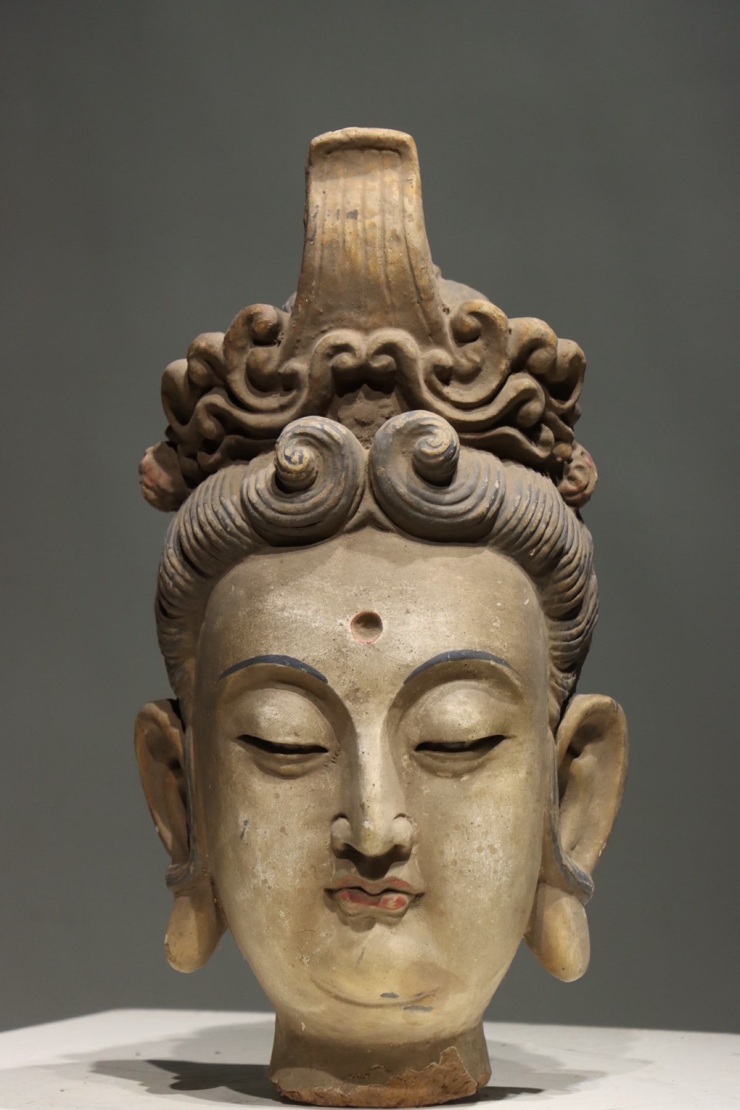 MING DYNASTY (15TH-17TH CENTURY) POLYCHROME CLAY HEAD OF AVALOKITESHVARA (GUANYIN): Height: 18.11" inches (46.0 cm)This exceptional polychrome clay head of Guanyin from the Ming Dynasty is a masterpiece of Chinese Han Buddhist art. It features a serene, compassionate countenance with