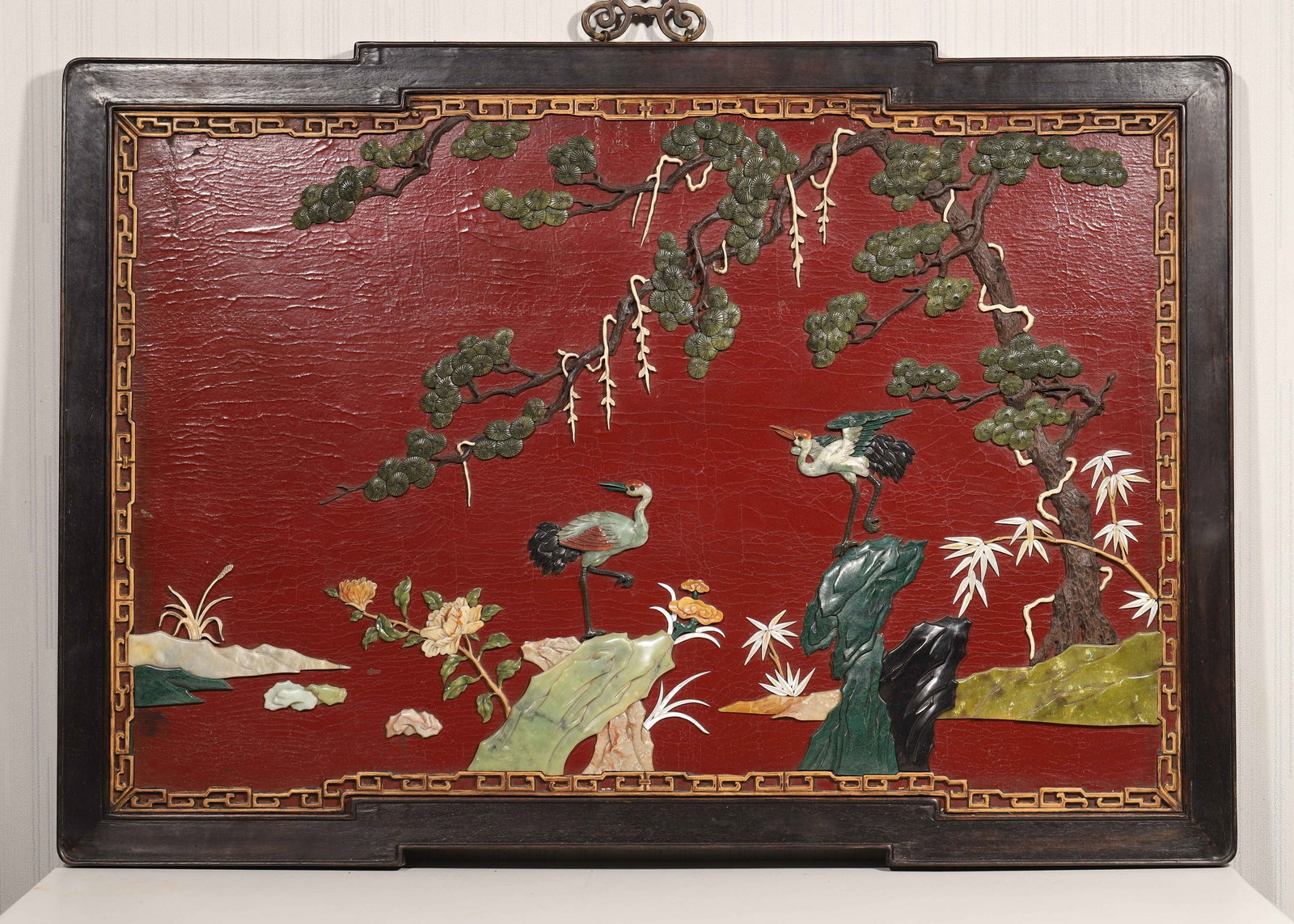 A ZITAN WOOD AND RED LACQUER WALL SCREEN INLAID WITH GEMSTONES, PINE AND CRANE MOTIF, QIANLONG: 35.38" x 25.25" (9.0cm x 64.0cm)This wall screen features a zitan wood frame, red lacquer background, and gemstone-inlaid "pine and crane" motif, bordered by gold-painted key patterns. Exquisitely cra