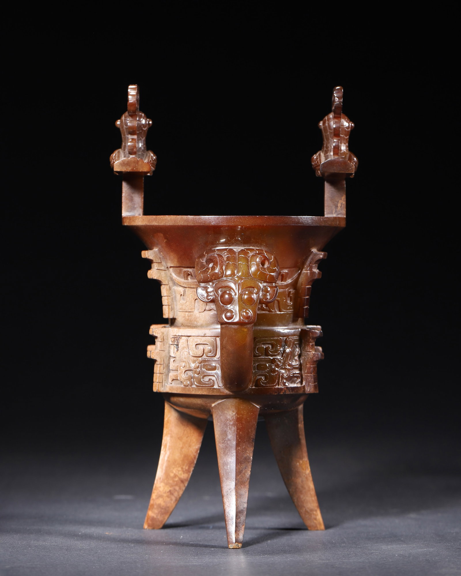 A WESTERN ZHOU DYNASTY (11TH-8TH CENTURY BC) NEPHRITE JIA VESSEL WITH TAOTIE MASKS AND PHOENIX: 3.94" x 8.27" inches (10.0 cm x 21.0 cm) | Weight: 1.3 lbs (590.0 g)This important ritual vessel, crafted from nephrite with rich red-brown patination, emulates a bronze jia. Its taotie masks and phoe