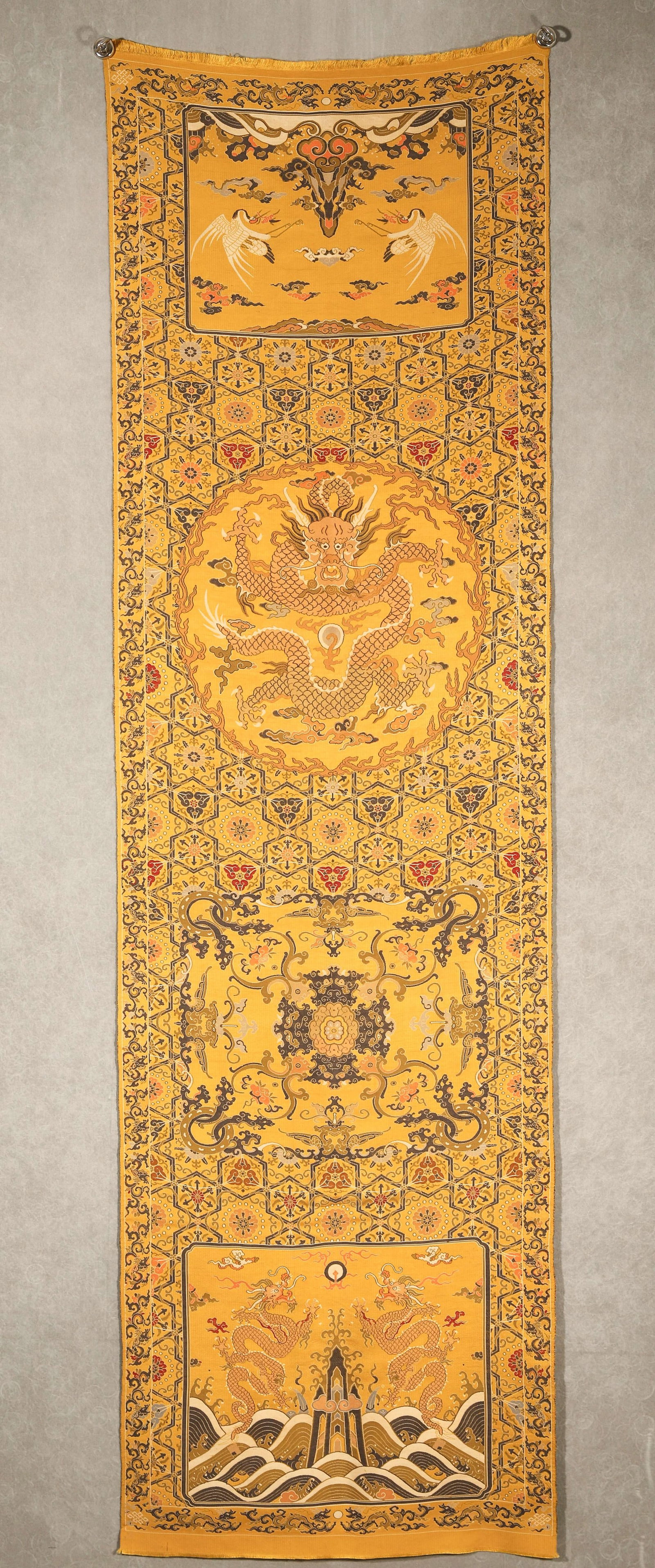 AN IMPORTANT IMPERIAL YELLOW KESI 'DRAGON AND CRANE' HANGING SCREEN, QING DYNASTY: L:177cm (69.69 in) W:52cm (20.47 in)A fine imperial yellow kesi hanging screen, Qing dynasty, woven with dragons, cranes, and waves, symbolizing longevity and imperial authority.