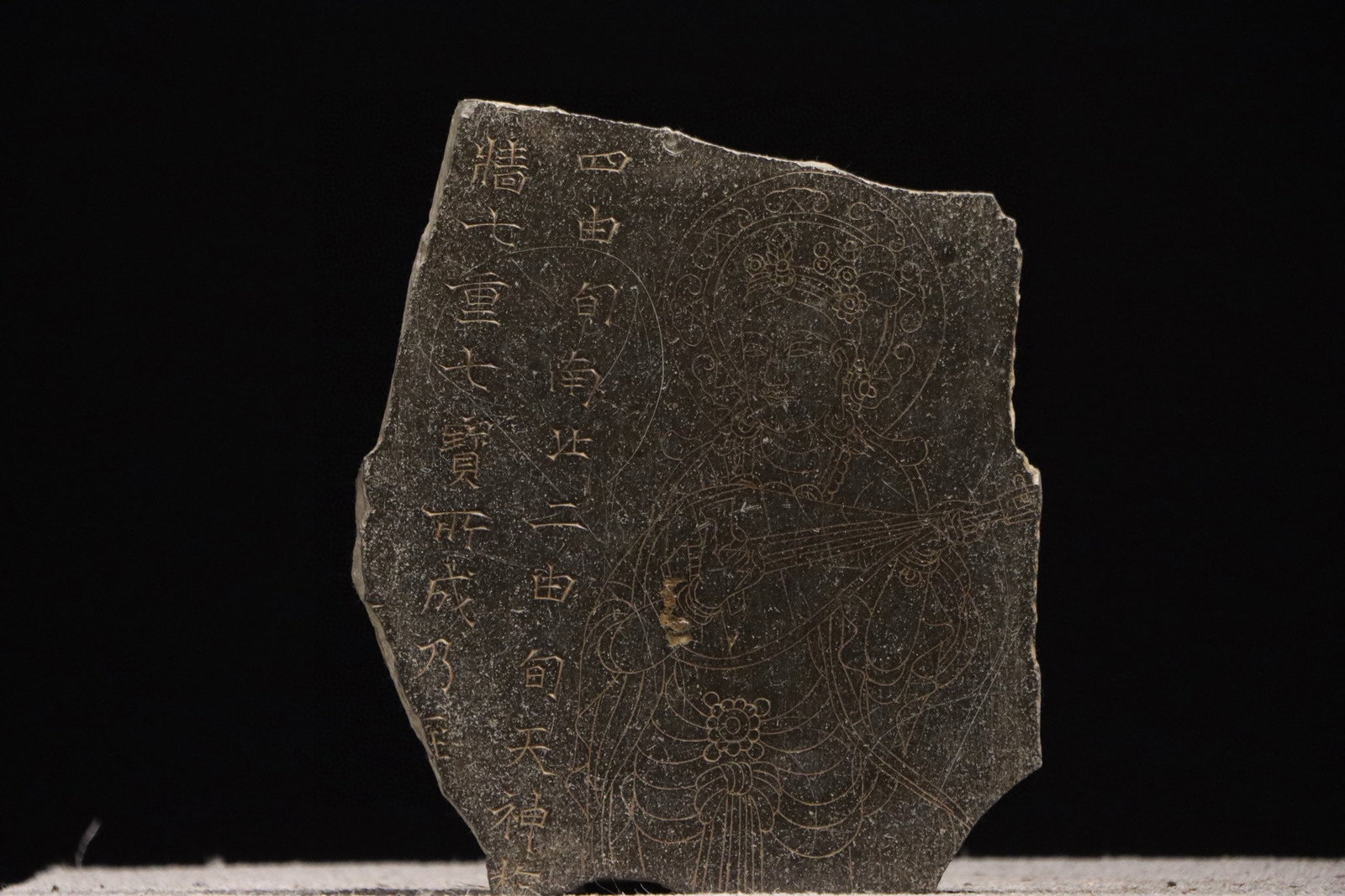 A GREY SCHIST STELE FRAGMENT WITH INCISED BUDDHIST FIGURE AND SCRIPTURE, TANG DYNASTY, 7TH–9TH: Height: 11.81" inches (30.0 cm) | Width: 9.84" inches (25.0 cm)This grey schist stele fragment from the Tang Dynasty (7th–9th century AD) features an incised pipa-bearing Bodhisattva with a gentle
