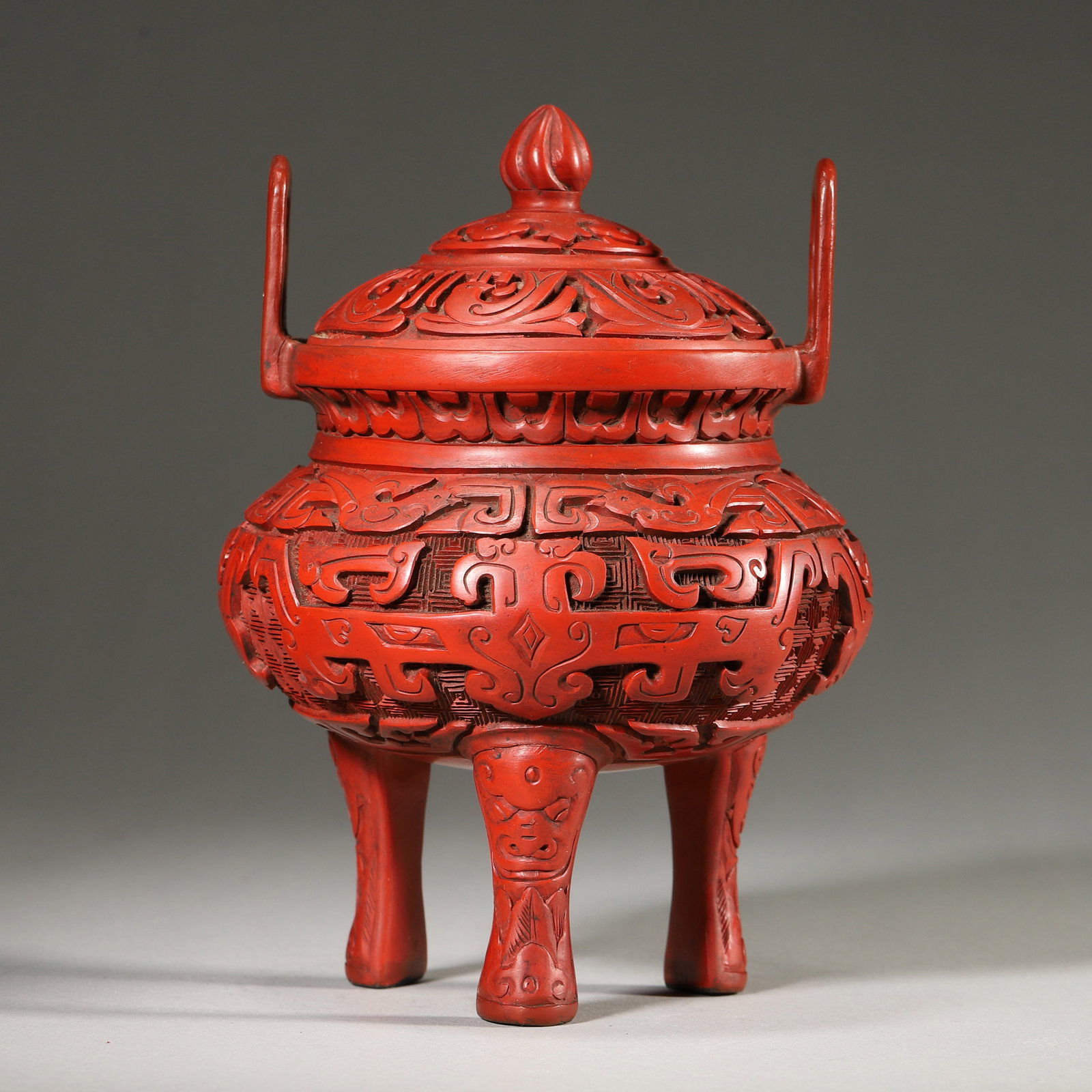 A Cinnabar Lacquer Censer with Taotie Motifs, Qing Dynasty: D 11.0cm (4.33 in); H 16.0cm (6.3 in); Wt 380.0g (0.84 lb)This tripod censer is carved from thick cinnabar lacquer in an archaic bronze form, with taotie patterns on a key-fret ground. It features upr