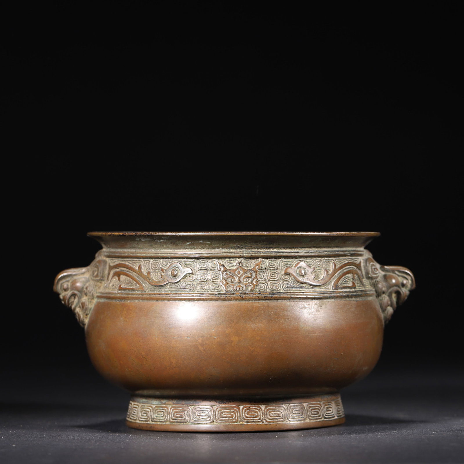 A Bronze Censer with Archaic Phoenix and Beast-Head Handles, Qing Dynasty: W 16.0cm (6.3 in); H 8.0cm (3.15 in); Wt 1238.0g (2.73 lb)This finely cast bronze censer features archaic phoenix motifs on the neck, beast-head handles, and a seal mark at the base. With rich patina 