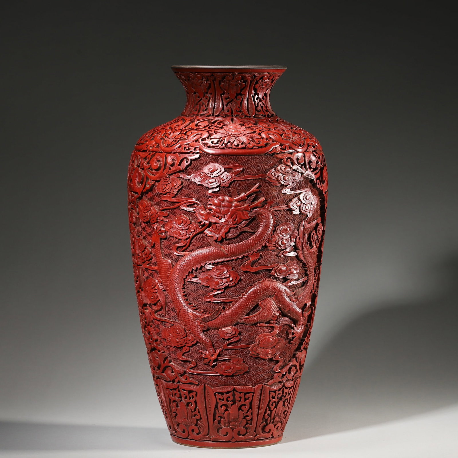A Cinnabar Lacquer Vase with Dragon and Cloud Motifs, Qing Dynasty: D 20.0cm (7.87 in); Wt 2304.0g (5.08 lb)This vase is carved from thick cinnabar lacquer with a rich red hue. It features a raised dragon and cloud motif on a key-fret ground, with lotus scrolls, exemp