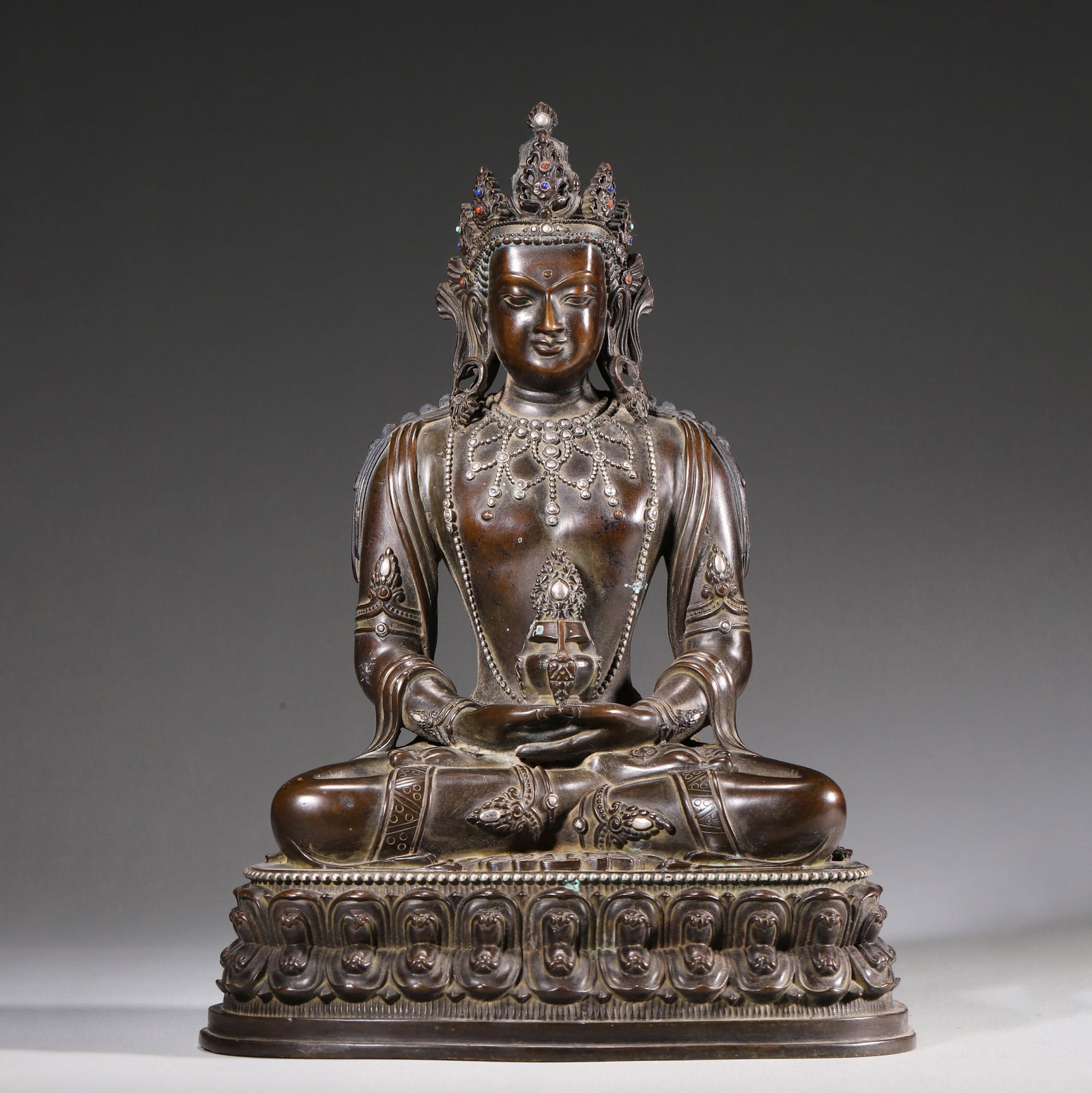 A Copper Figure of Amitayus with Silver Inlay, Qing Dynasty: H 24cm (9.45 in); L 17cm (6.69 in); W 13cm (5.12 in); Wt 2441g (5.38 lb)A finely cast copper figure of Amitayus, with mellow patina and partial silver inlay. Adorned with a gem-set crown, the Buddha h