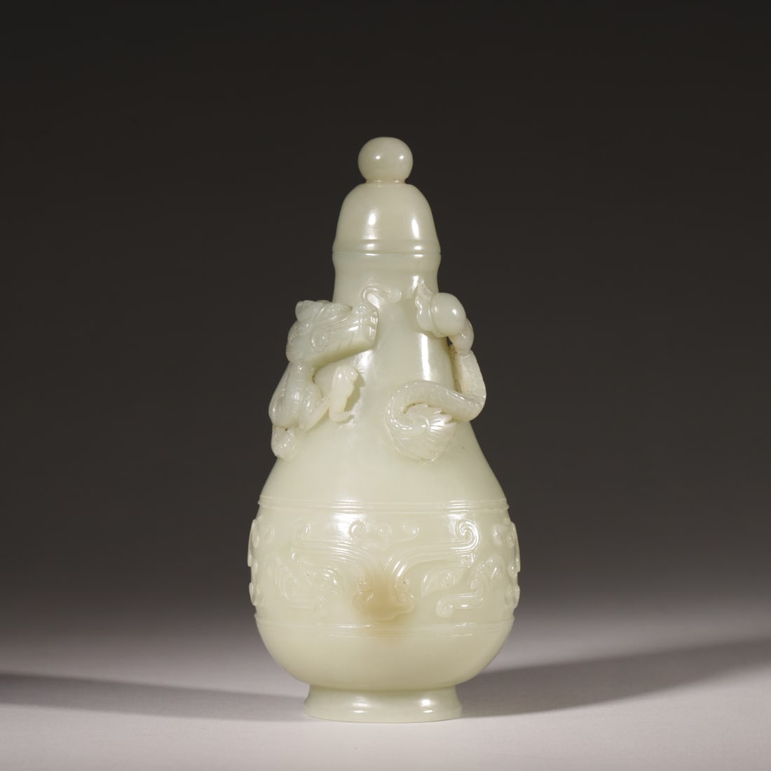 A Hetian White Jade Vase with Raised Dragon Carving, Qing Dynasty: D 7.0cm (2.76 in); H 16.0cm (6.3 in); Wt 273.0g (0.6 lb)This vase is carved from a single piece of fine Hetian white jade, featuring a raised dragon on the shoulder and archaic beast motifs on the bod