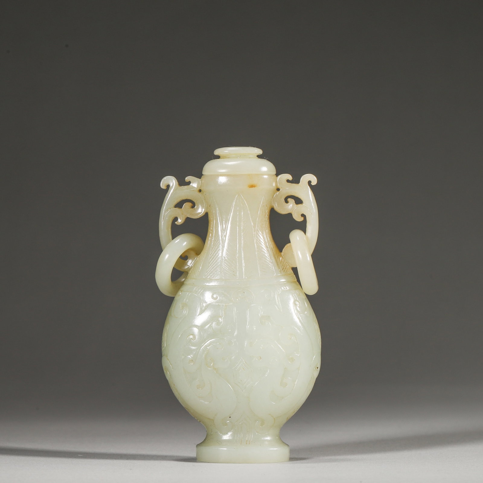 A Hetian White Jade Vase with Loose-Ring Handles, Qing Dynasty: L 4.9cm (1.93 in); W 2.8cm (1.1 in); H 10.0cm (3.94 in); Wt 123.0g (0.27 lb)This vase is carved from a single piece of fine Hetian white jade, featuring loose-ring handles and archaic dragon motifs. W