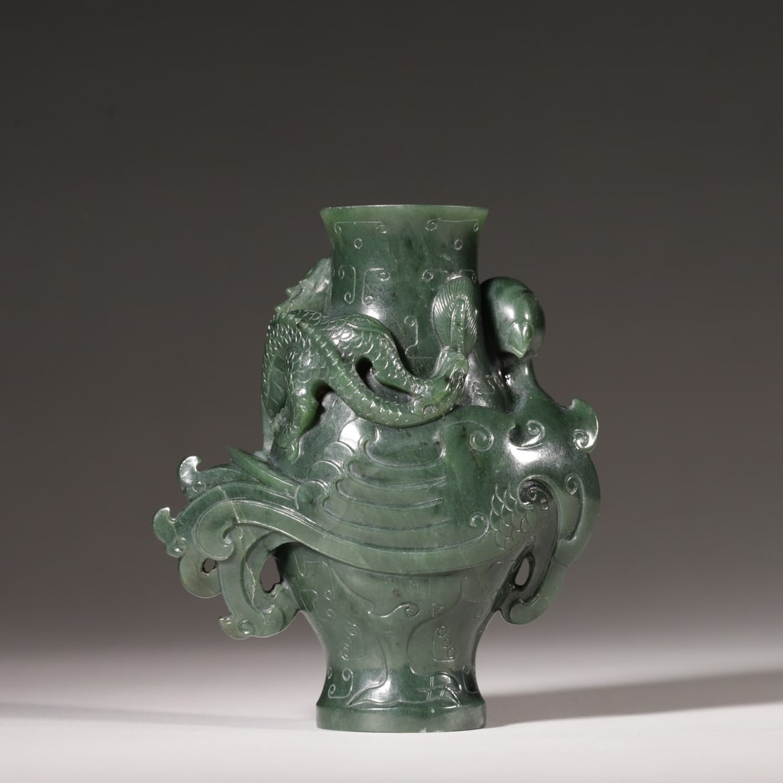 A Hetian Green Jade Dragon and Phoenix Vase, Qing Dynasty: L 9.0cm (3.54 in); W 4.0cm (1.57 in); H 10.5cm (4.13 in); Wt 311.0g (0.69 lb)This vase is carved from a single piece of fine Hetian green jade, featuring a raised dragon and phoenix motif, symbolizing