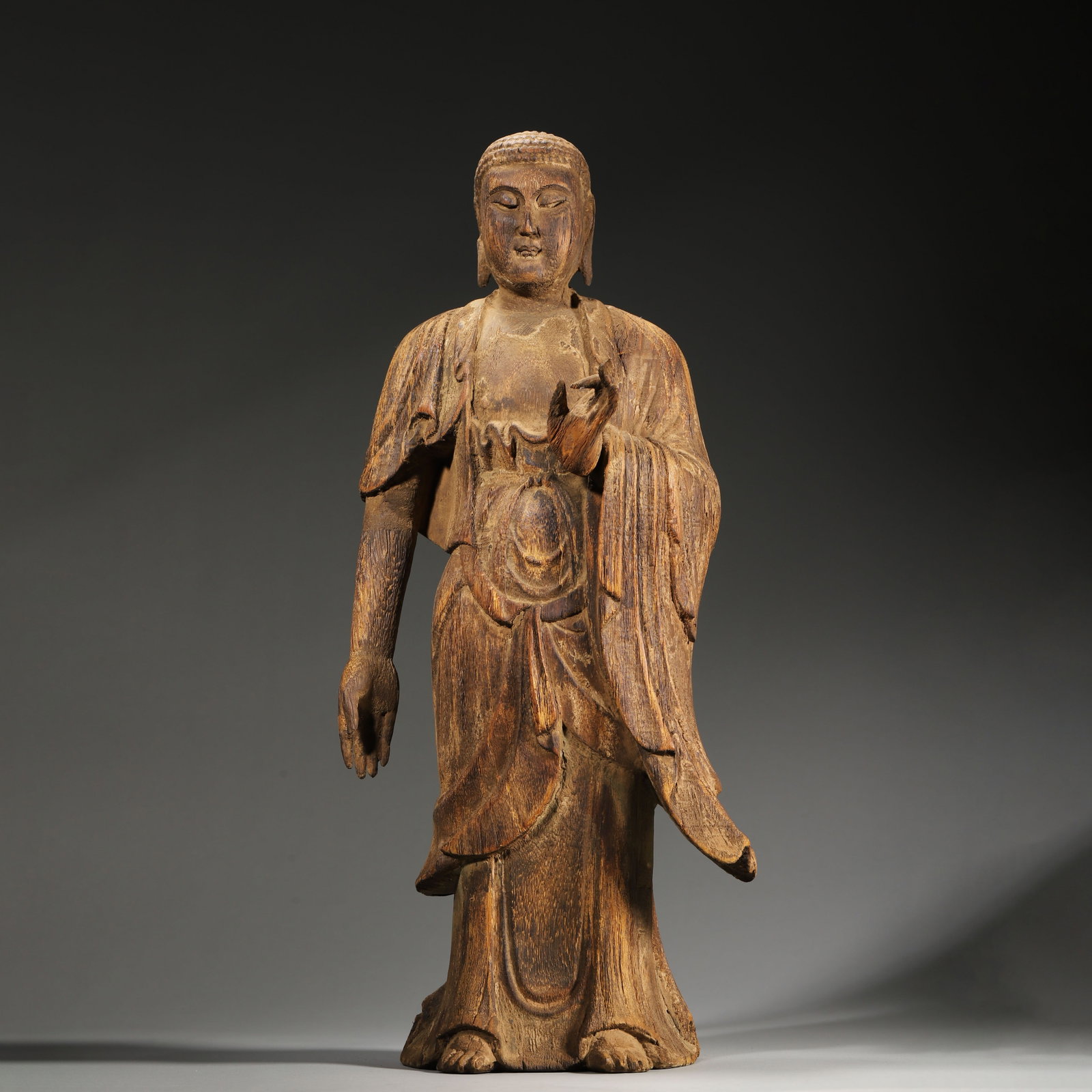 A Wooden Standing Statue of Sakyamuni, Song Dynasty: L 20.0cm (7.87 in); W 14.0cm (5.51 in); H 45.0cm (17.72 in); Wt 1041.0g (2.3 lb)This wooden standing statue of Sakyamuni is carved from a single piece of wood, with a serene face and flowing robes, re