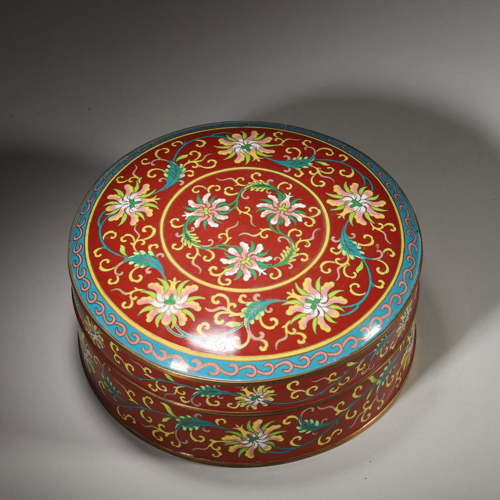 A Copper-Body Painted Enamel Box with Floral Scroll Design, Qing Dynasty: D 22.0cm (8.66 in); H 10.0cm (3.94 in); Wt 1450.0g (3.2 lb)A copper-body painted enamel box of the Qing Dynasty, decorated with vibrant floral scroll designs on a red ground. The interior is covered w