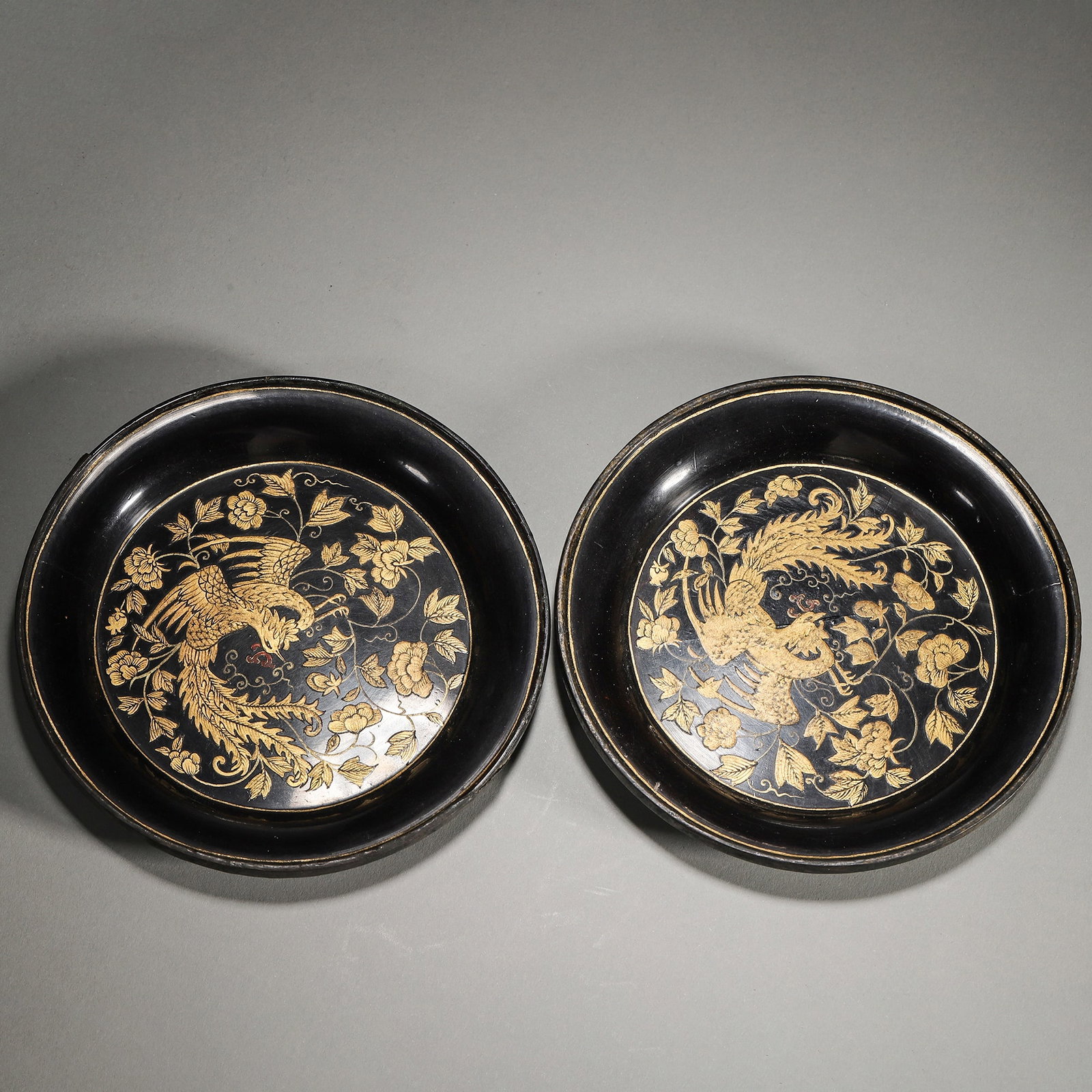 A Pair of Black Lacquer Dishes with Gilt Phoenix and Peony Design, Qing Dynasty: D 13.0cm (5.12 in); Wt 100.0g (0.22 lb)A pair of black lacquer dishes of the Qing Dynasty, featuring gilt phoenix and peony patterns on the center. The phoenix and peony design symbolizes prosperity a