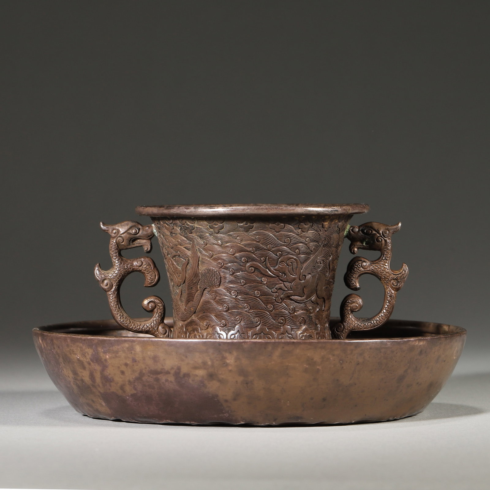 A Set of Silver Cup and Saucer with Dragon Handles and Sea Creature Design, Ming Dynasty: D 12.5cm (4.92 in); H 6.0cm (2.36 in); Wt 257.0g (0.57 lb)A set of silver cup and saucer from the Ming Dynasty. The cup features finely chiseled sea creatures amid waves, flanked by powerful dragon ha