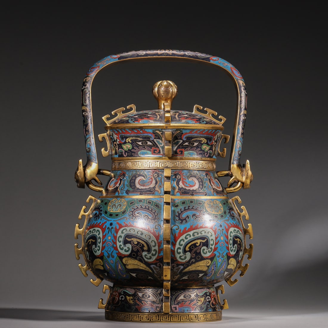 A Cloisonné Bronze You with Taotie Design, Marked "Made in Qianlong Period", Qing Dynasty: H 32cm (12.60 in); L 22cm (8.66 in); W 20cm (7.87 in); Wt 3773g (8.32 lb)A cloisonné bronze you of the Qianlong period, imitating the Shang-Zhou ritual form. Gilt overall, with fine cloisonné inlaid
