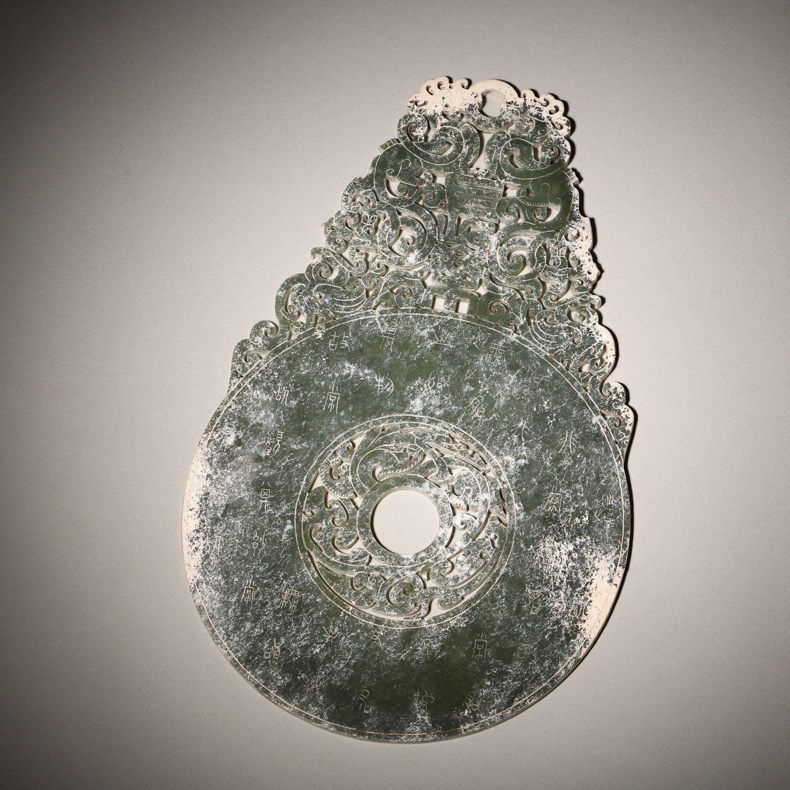 A RARE HETIAN CELADON JADE OPENWORK "CHANGLE" INSCRIBED BI DISC WITH DOUBLE DRAGONS, HAN DYNASTY: L: 24.5cm (9.65in) W: 15.5cm (6.10in) Weight: 262.6g (0.58lb)This rare Han Dynasty Hetian celadon jade bi disc features openwork double dragons, "Changle" inscription, and seal script text. A masterpi